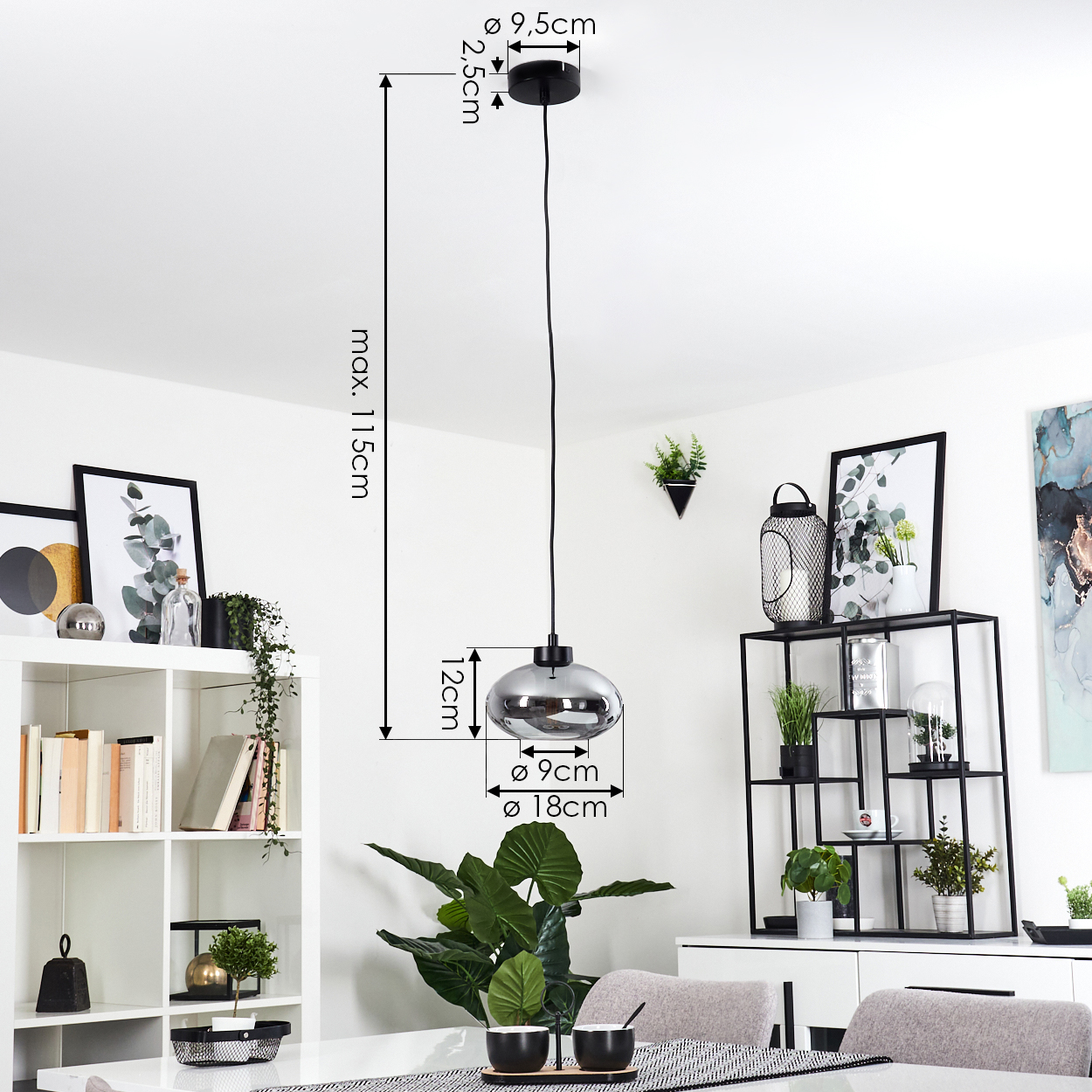 Eine Pendelleuchte mit beschrifteten Maßen hängt über einem Tisch mit schwarzen Schalen. Regale zeigen Pflanzen und Kunstwerke.