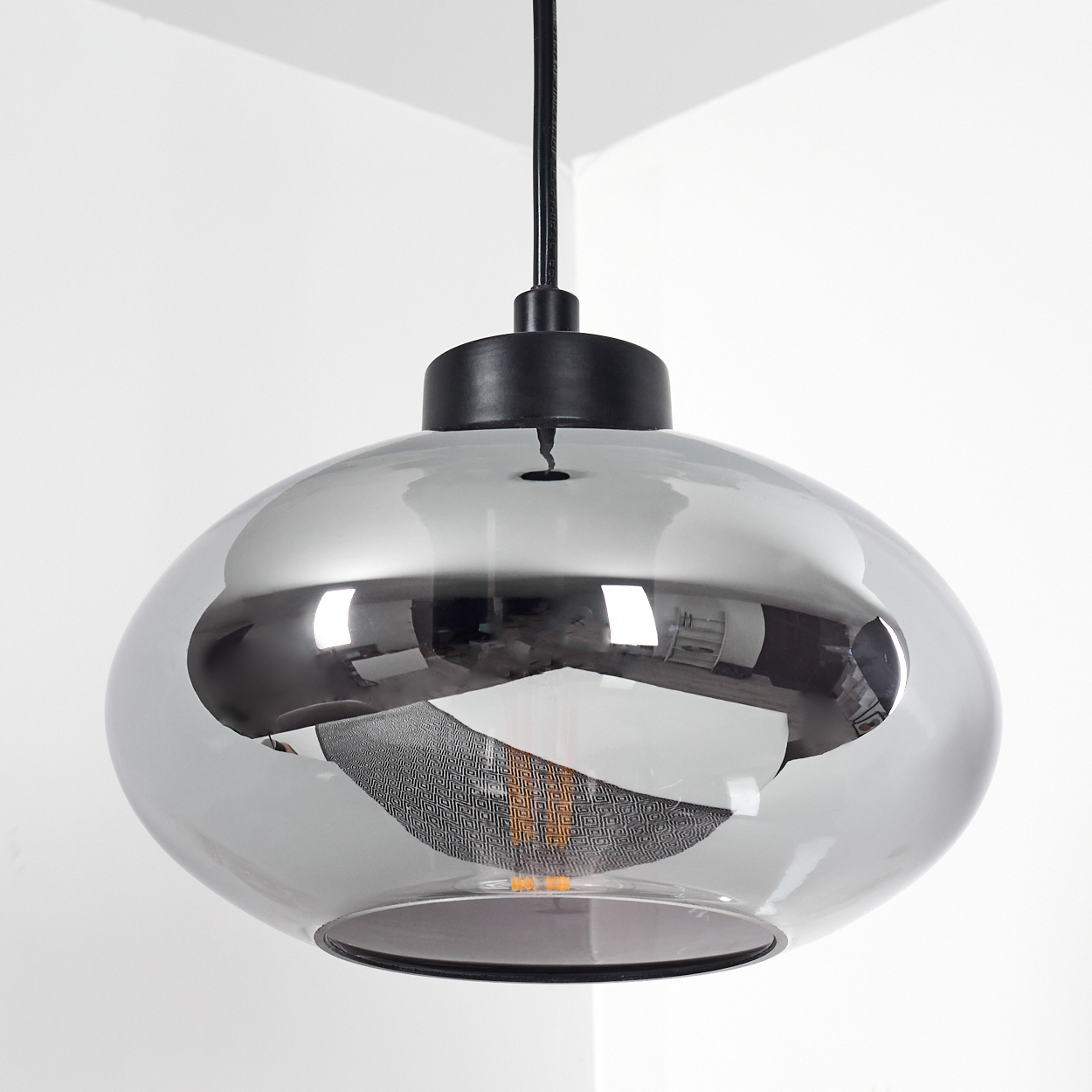 Eine moderne, kugelförmige Pendelleuchte mit rauchfarbenem Glasschirm hängt an einem schwarzen Kabel vor einer weißen Wand.