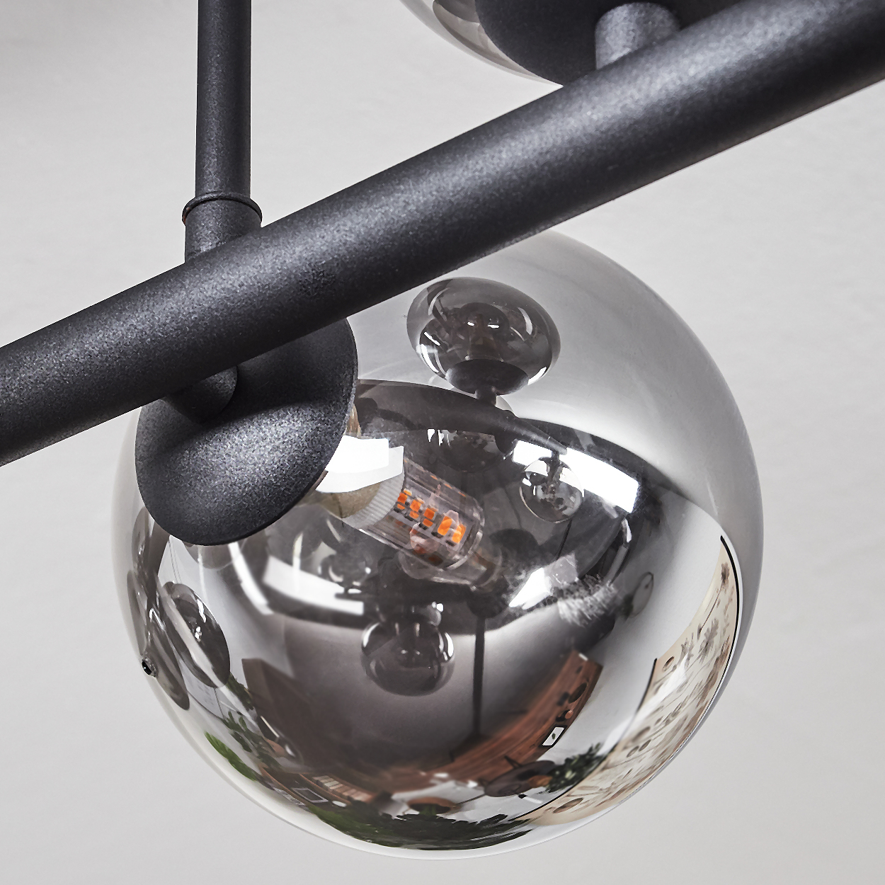 Nahaufnahme einer modernen Deckenlampe. Sie hat schwarze Metallstangen und kugelförmige, verspiegelte Glasschirme, die die Umgebung reflektieren.