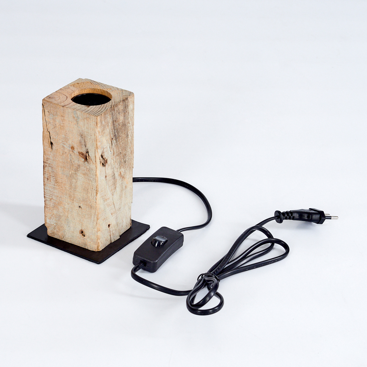 Eine Holzlampen mit schwarzem Sockel und Kabel. Die Lampe ist rechteckig, mit einem Loch oben. Das Kabel hat einen Schalter und einen Stecker.