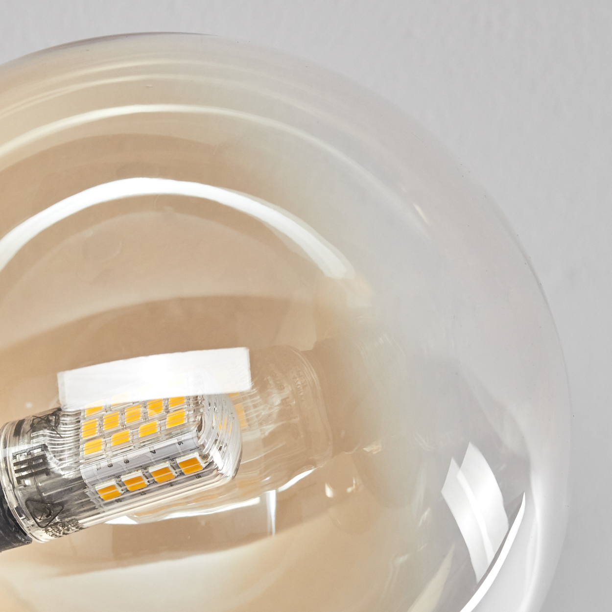 Nahaufnahme einer Glühbirne. Die Birne ist ein großes, klares Glas mit einem warmen Bernsteinton. Der Sockel zeigt die LED-Leuchten.