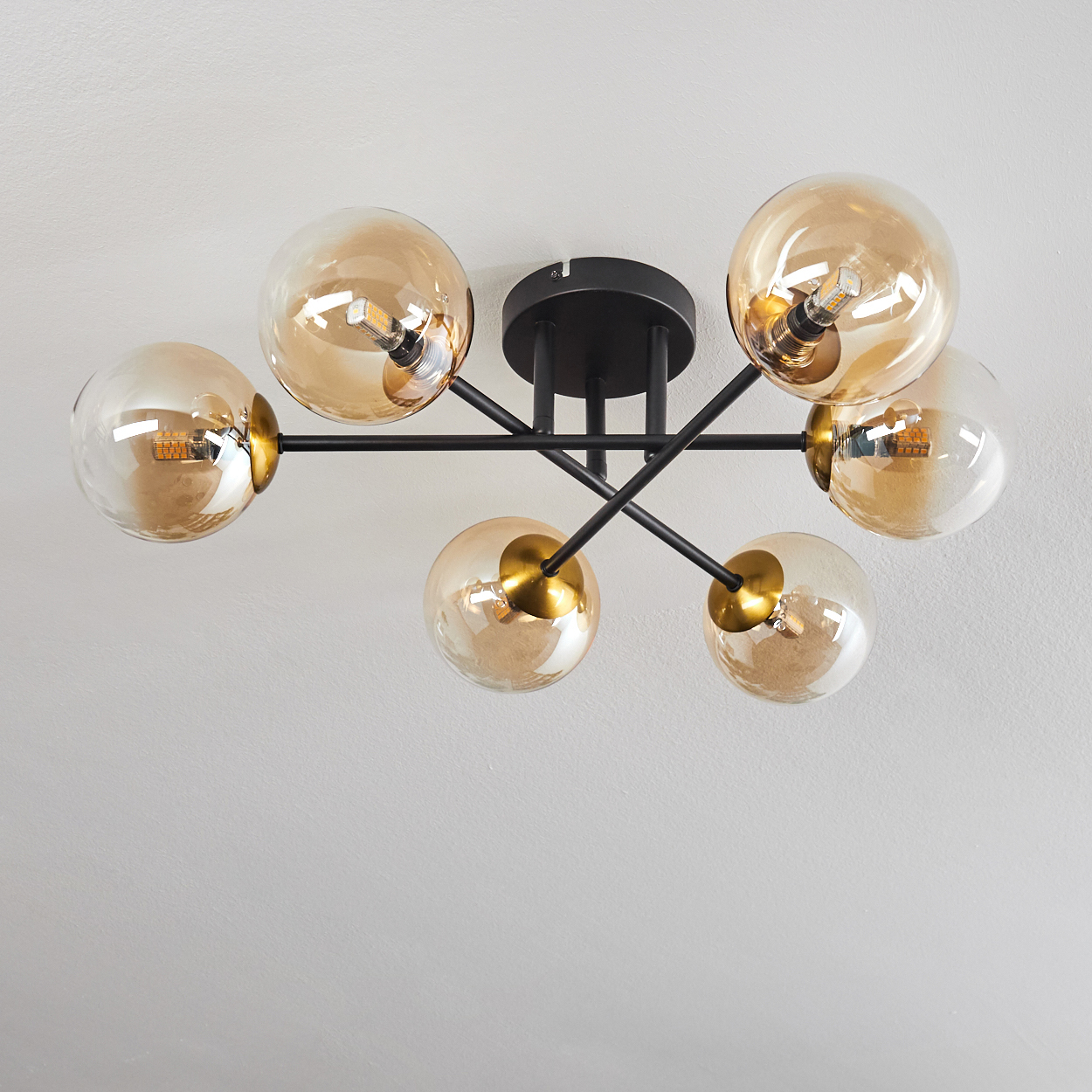 Moderne Deckenleuchte mit sechs bernsteinfarbenen Glaskugeln und schwarzen Metallarmen an weißer Decke.