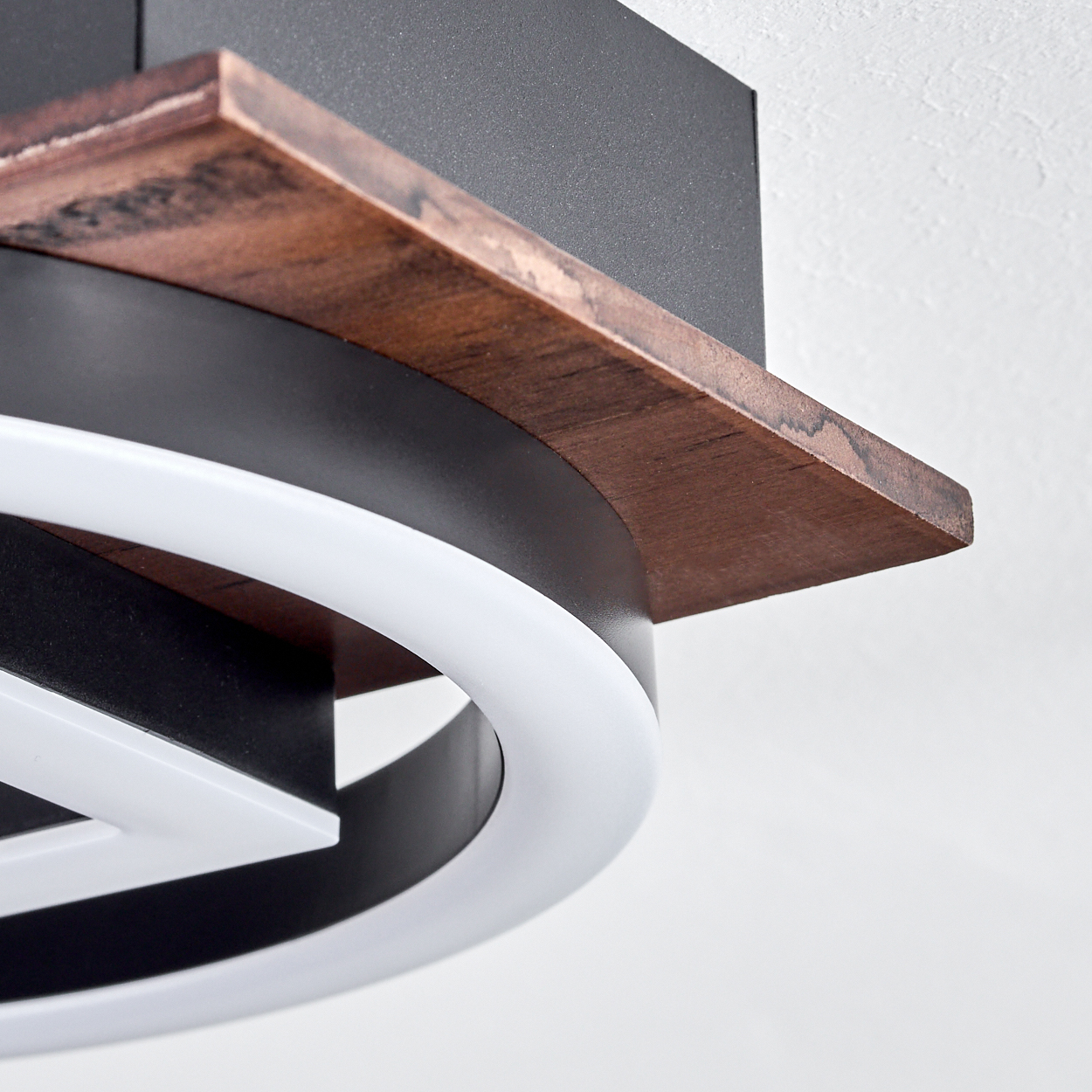 Nahaufnahme einer modernen Deckenleuchte. Mit Holzregal, schwarzem Rahmen und weißem LED-Ring. Hintergrund ist eine weiße Decke.