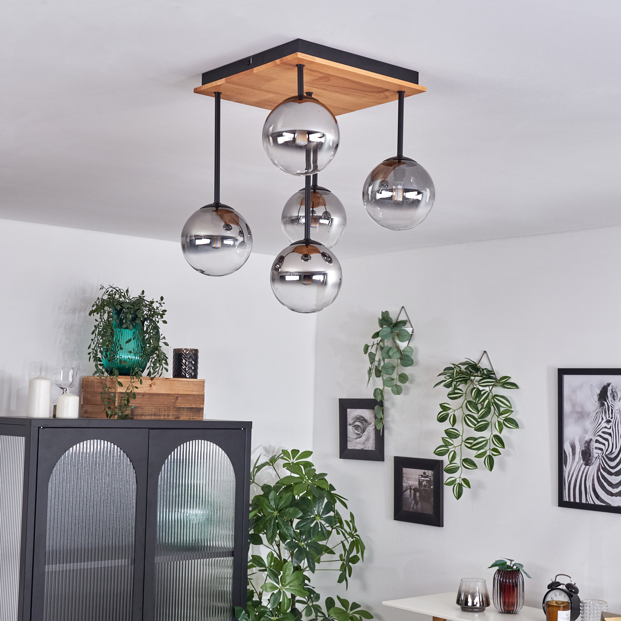 Modernes Zimmer mit Deckenlampe, Möbeln, Pflanzen und gerahmten Bildern. Rechts ist ein Zebra-Bild.