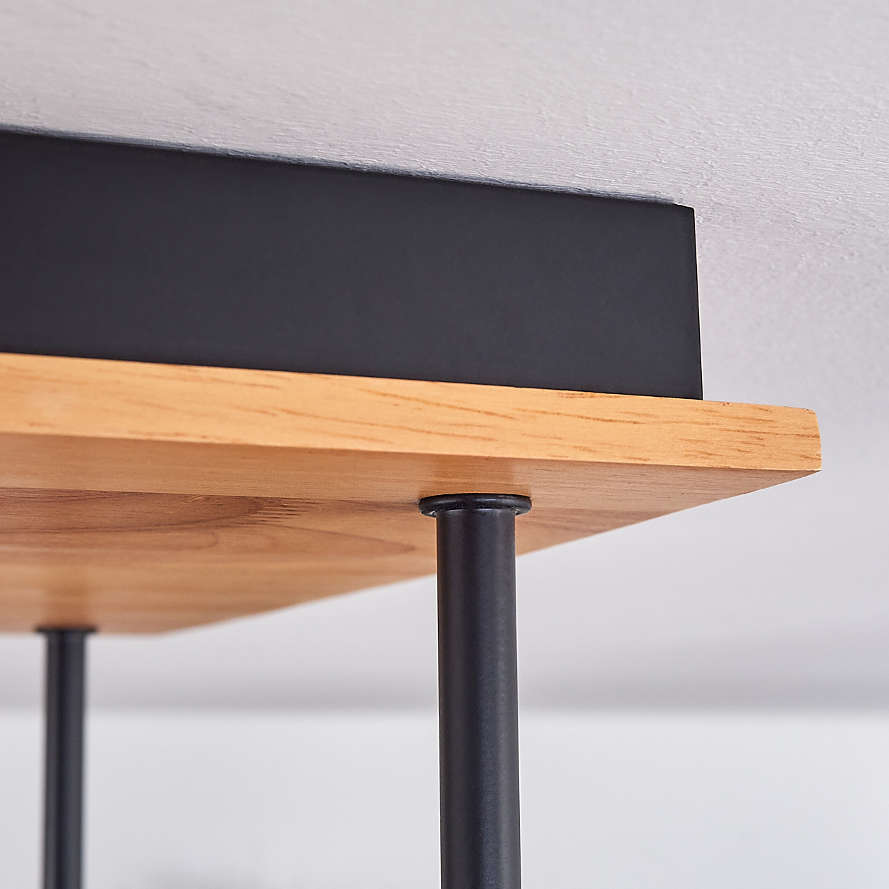 Nahaufnahme eines Holzregals mit schwarzen Stützen. Über dem Regal befindet sich eine schwarze Box. Weißer Hintergrund.