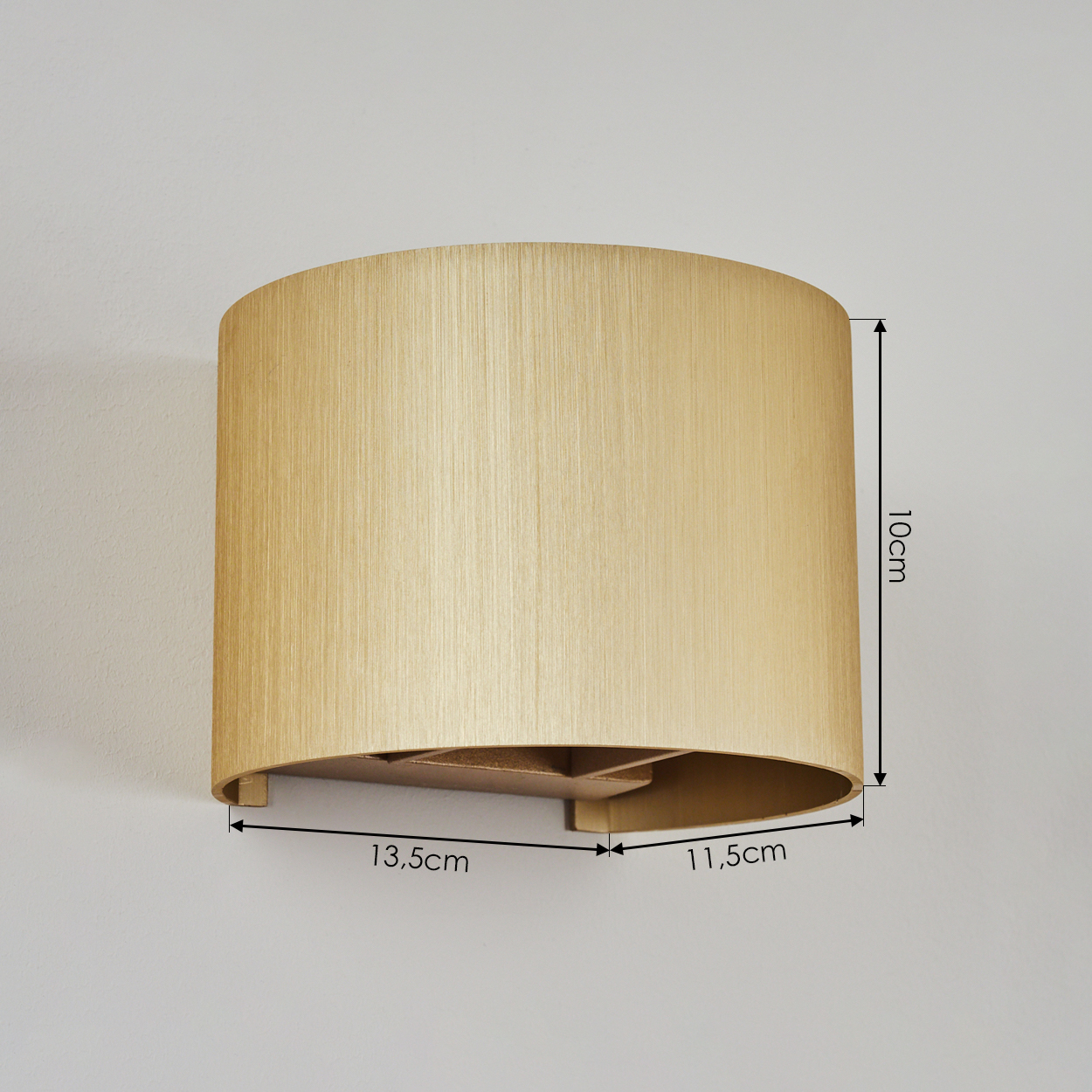 Eine Wandlampe mit beigem Lampenschirm ist an einer weißen Wand montiert. Maße sind markiert: 10cm hoch, 13,5cm und 11,5cm breit.