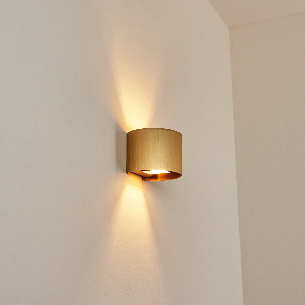 Eine goldene zylindrische Wandleuchte ist an einer weißen Wand montiert. Licht scheint nach oben und unten.