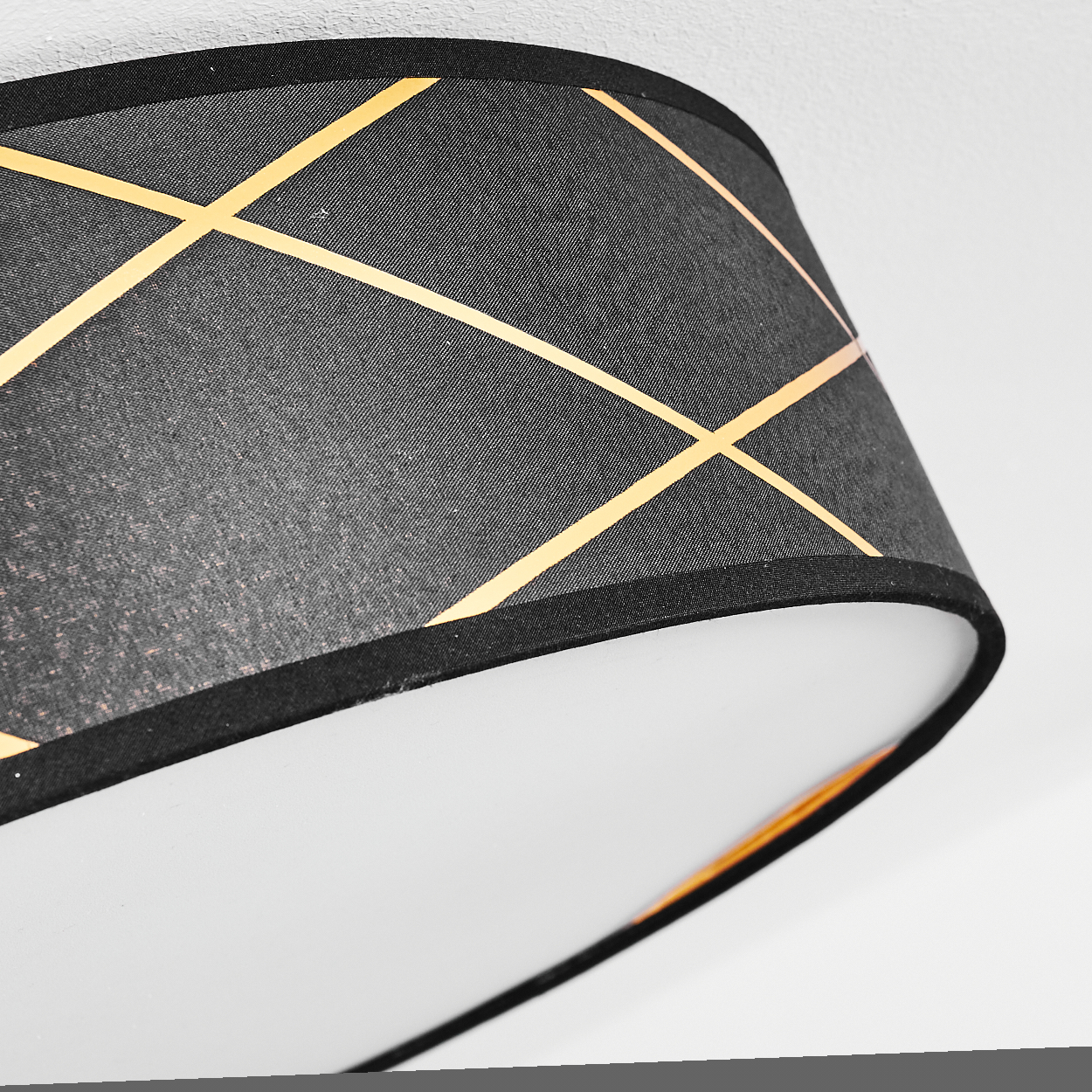 Nahaufnahme eines Lampenschirms mit schwarzer Außenseite, goldenen diagonalen Linien und weißer Innenseite auf weißem Hintergrund.