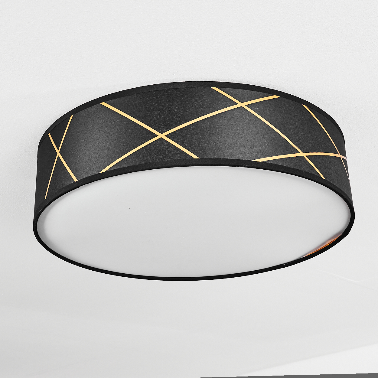 Eine schwarze Deckenlampe mit goldenem Gittermuster auf dem Schirm und einem weißen Diffusor. Die Lampe ist an einer weißen Decke montiert.