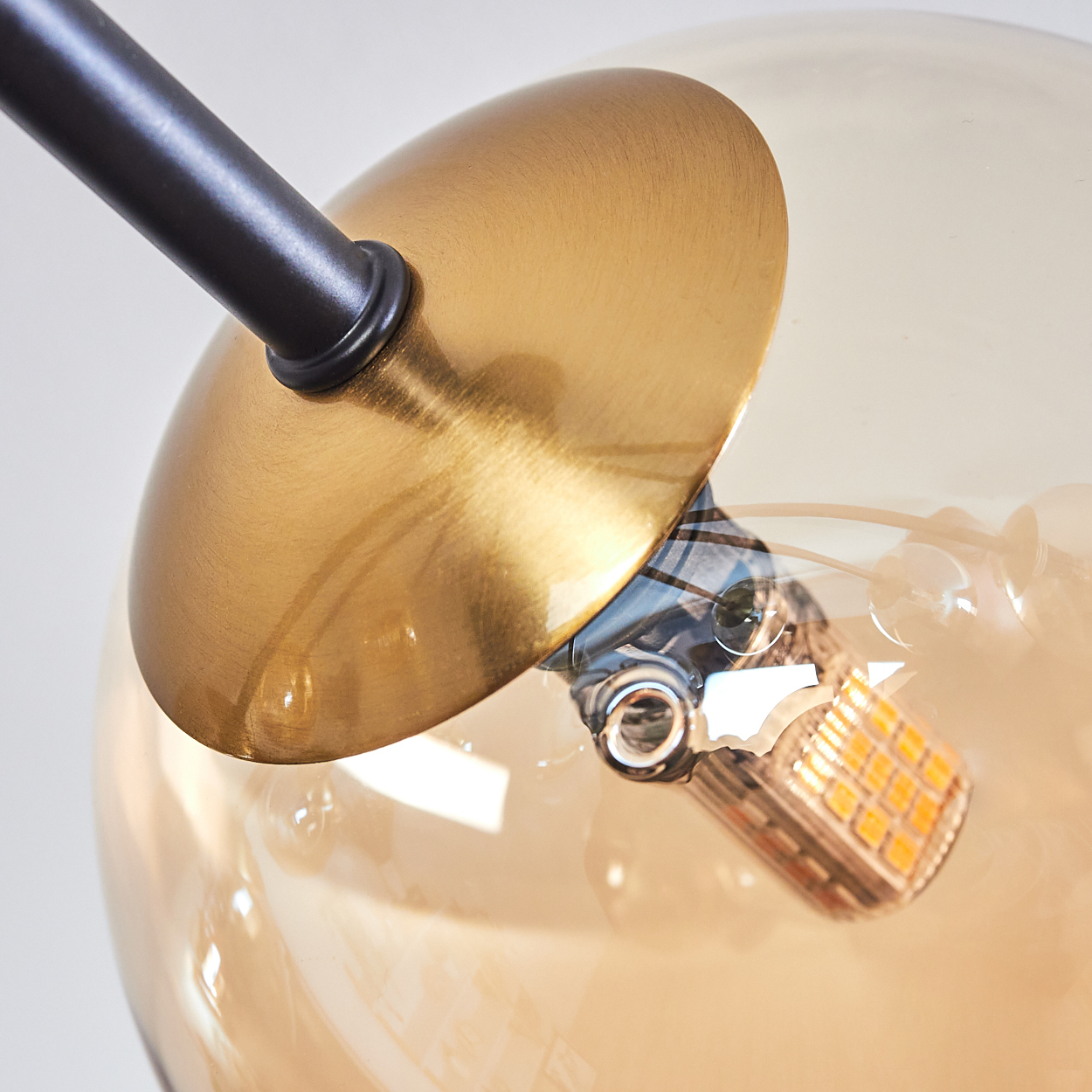 Nahaufnahme einer modernen Lampe. Sie hat einen goldenen Schirm, einen schwarzen Arm und einen klaren Globus, der eine warme LED-Lichtquelle umschließt.