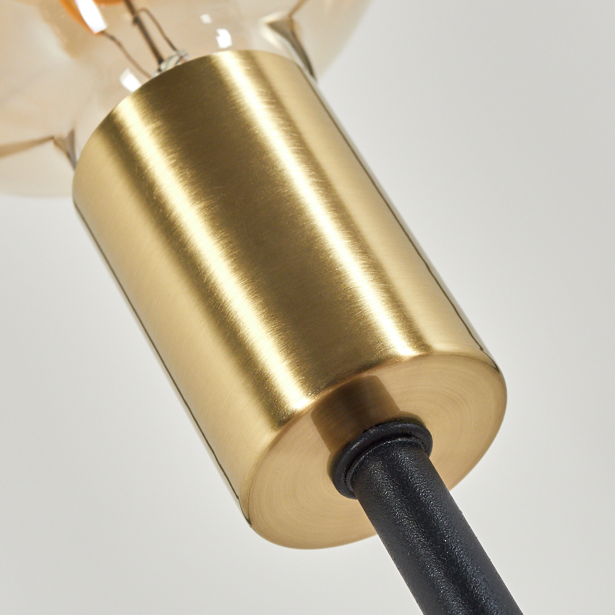 Nahaufnahme eines goldfarbenen Metalllampenhalters, der an einer schwarzen Stange befestigt ist. Oben ist eine Glühbirne vor weißem Hintergrund zu sehen.