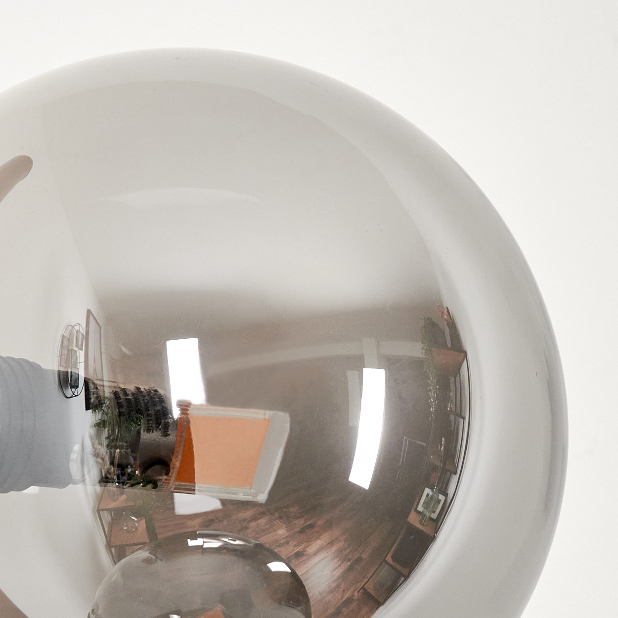 Eine große, reflektierende, graue Glühbirne mit Reflexionen eines Raumes, einschließlich Holzboden, Möbeln und weißer Wand.