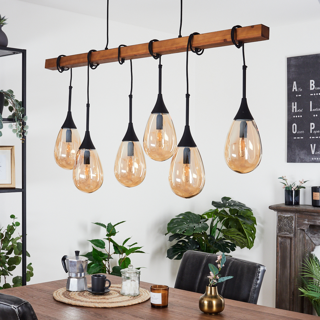 Ein Esszimmer mit Holztisch, Kronleuchter mit sechs Pendelleuchten und Pflanzen. Kaffeemaschine und Kerze sind sichtbar.