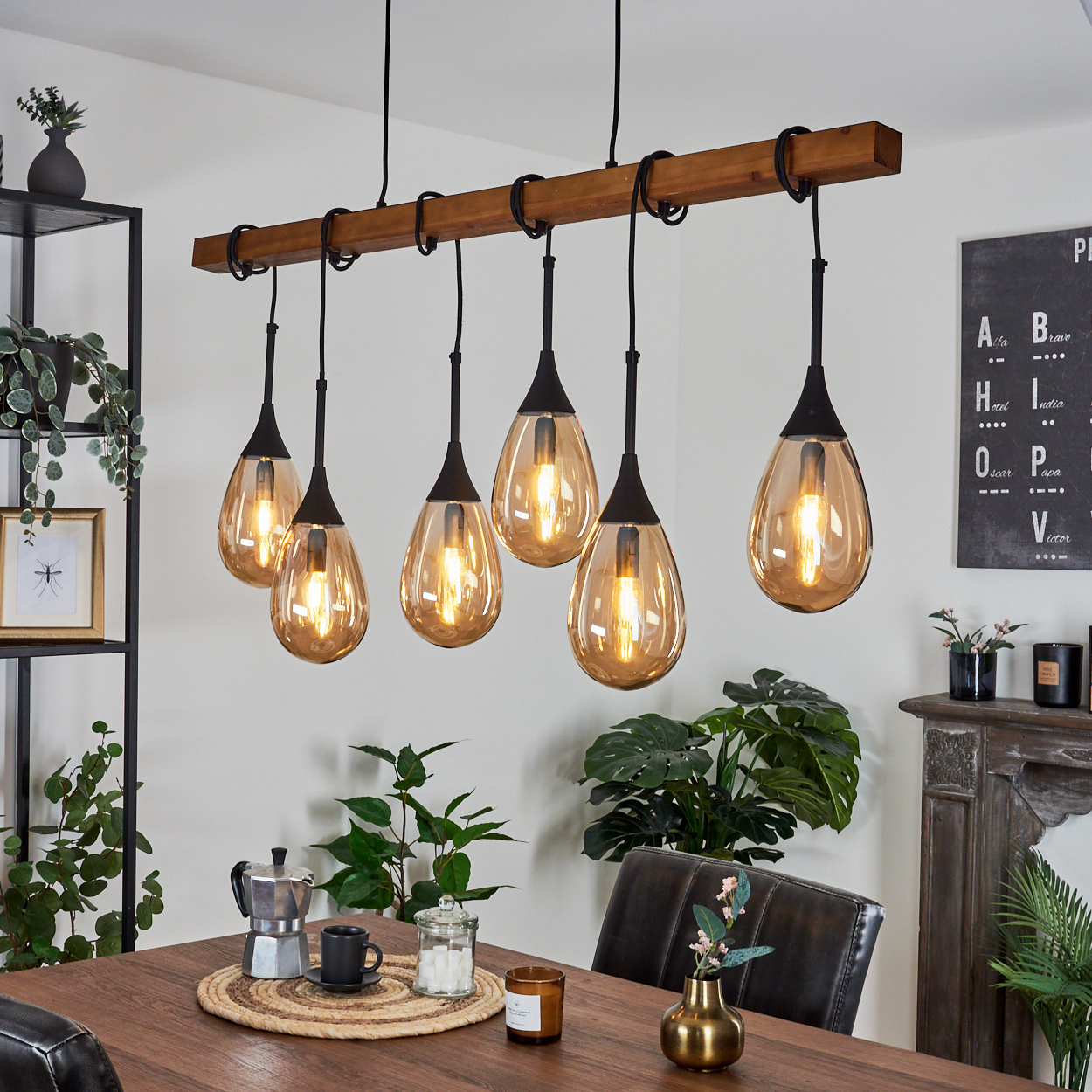 Ein Esszimmer mit Holztisch. Sechs tropfenförmige Lampen hängen von einem Holzbalken. Pflanzen und Dekoration sind sichtbar.