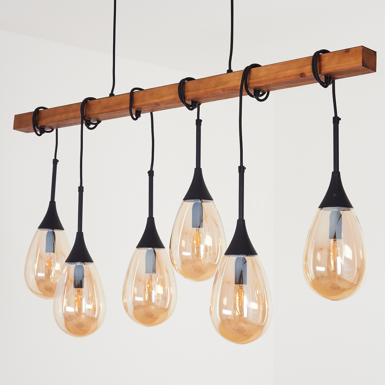 Ein Holzbalken mit sechs tropfenförmigen Pendelleuchten. Jede Leuchte hat eine schwarze Halterung und eine warm getönte Glühbirne.