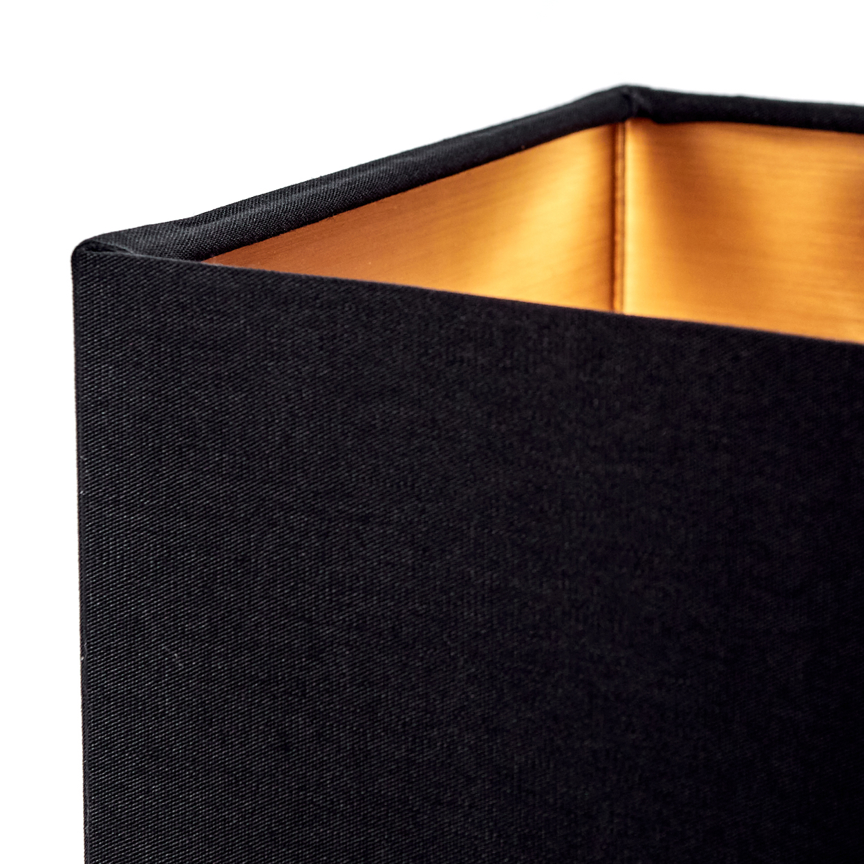 Nahaufnahme eines schwarzen Lampenschirms. Die Innenseite ist goldfarben, der Stoff außen schwarz. Die Ecke ist vor weißem Hintergrund sichtbar.