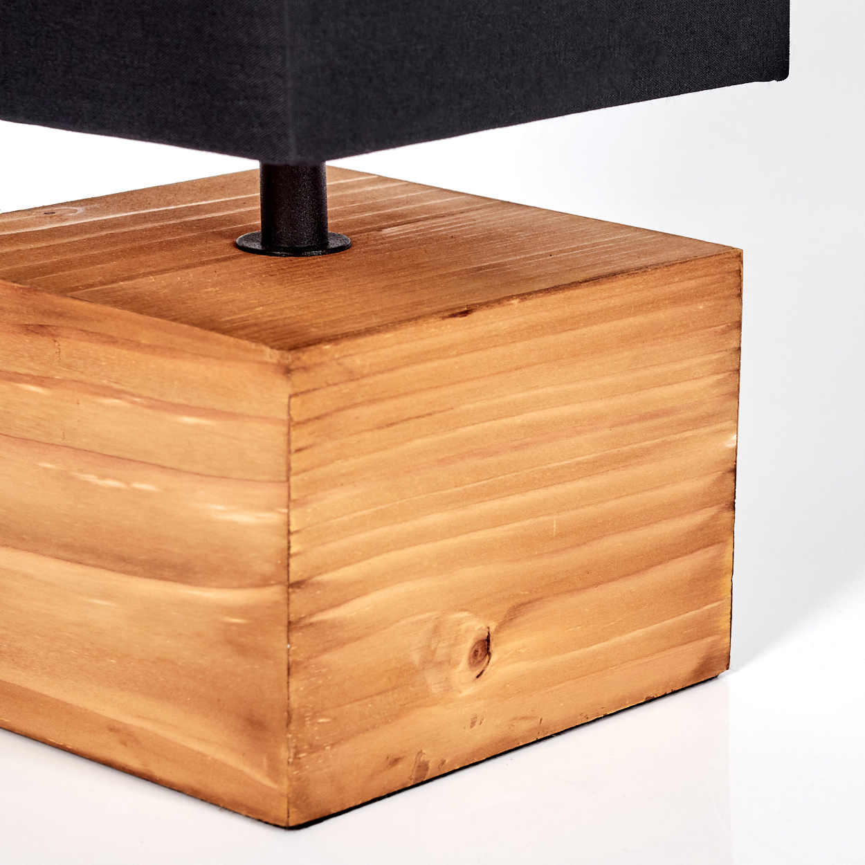 Nahaufnahme einer Lampe. Sie hat einen schwarzen Lampenschirm über einem Holzsockel. Der Sockel hat eine quadratische Form aus hellbraunem Holz.