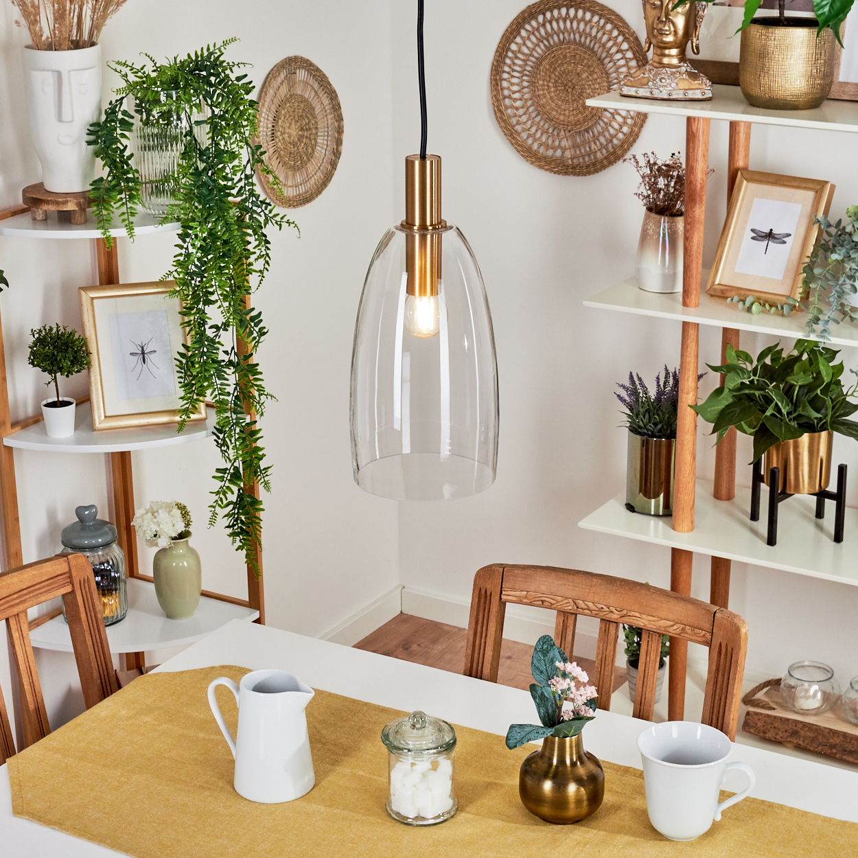 Ein Esszimmer mit einer Glas-Pendelleuchte, Tisch mit gelbem Läufer, Pflanzen und Dekorationsartikeln auf Regalen.
