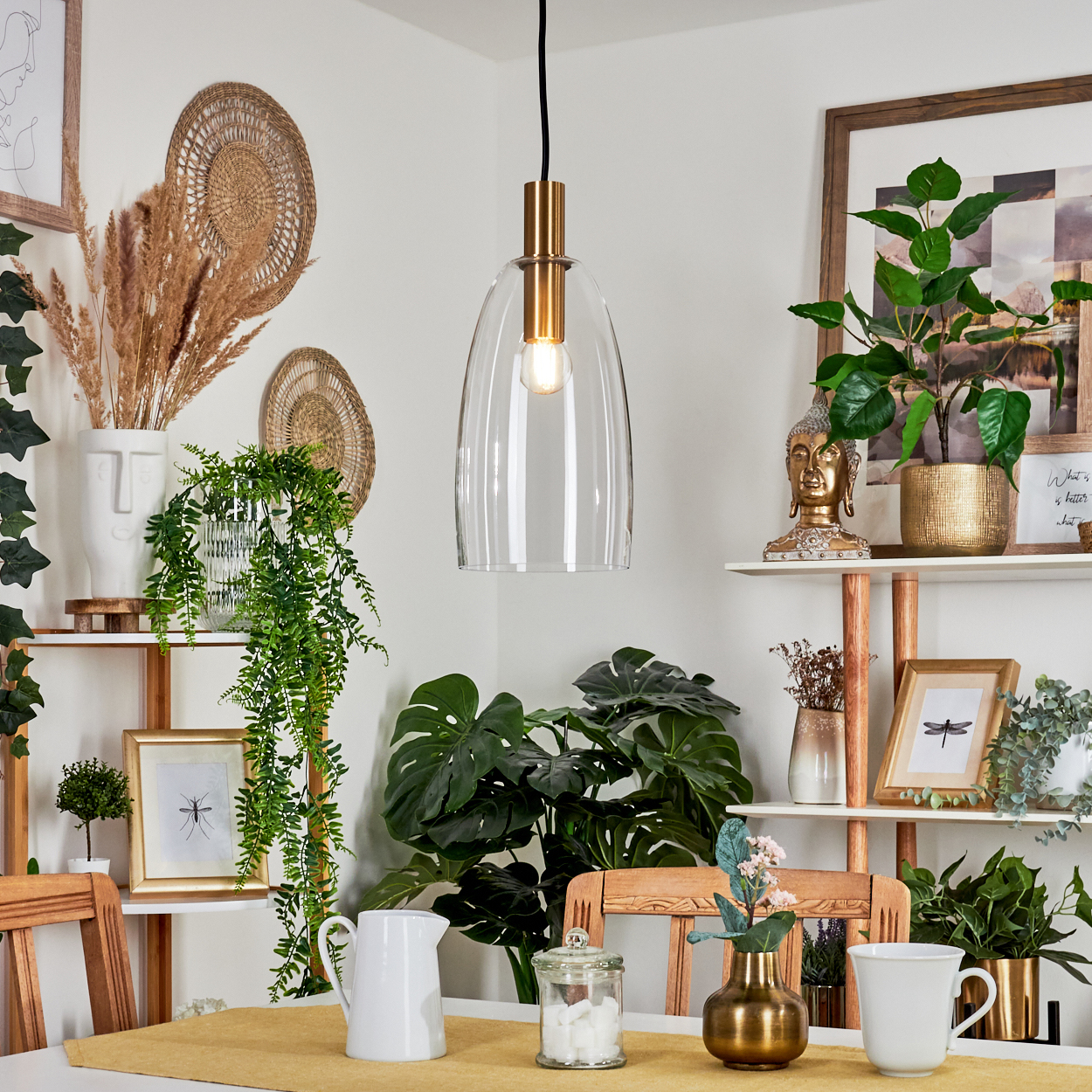 Ein Esszimmer mit einer klaren Glas-Hängelampe, Pflanzen und einem weißen Tisch mit gelbem Läufer. Regale zeigen Dekoration.