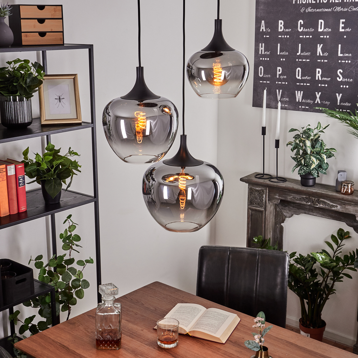 Drei Pendelleuchten hängen über einem Tisch mit einem Buch und einem Glas. Regale mit Pflanzen und ein dekorativer Kamin im Hintergrund.