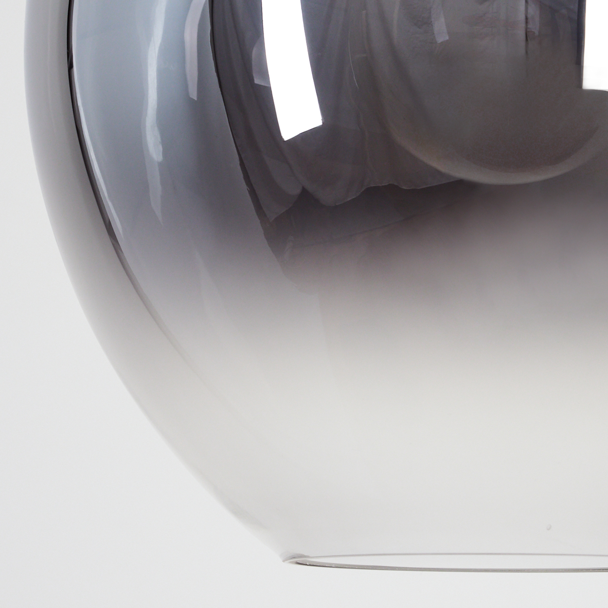 Nahaufnahme eines gläsernen Lampenschirms mit Farbverlauf von Grau zu Weiß. Das Glas reflektiert Licht, helle weiße Formen.