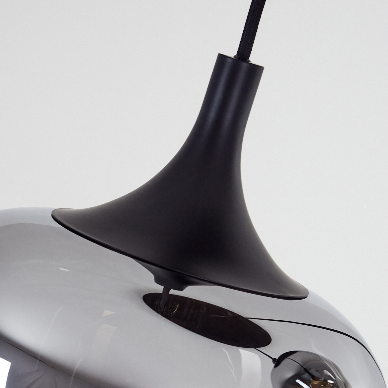 Nahaufnahme einer modernen Lampe. Sie hat einen schwarzen Deckel und einen reflektierenden, silberfarbenen Boden. Ein schwarzes Kabel hängt von oben.