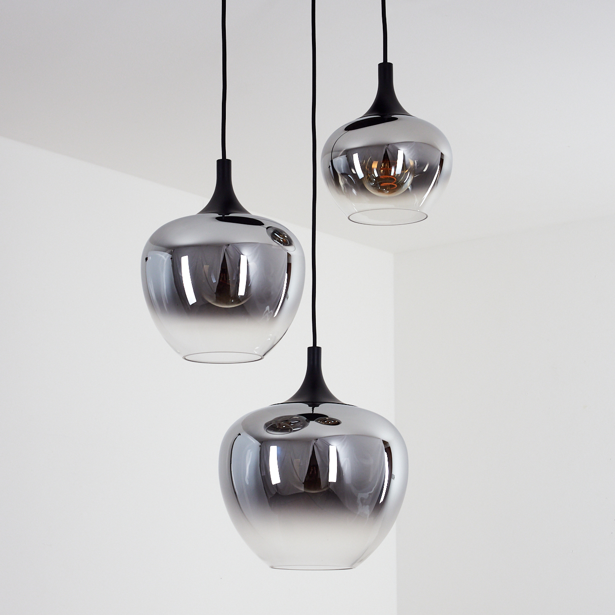 Drei moderne Pendelleuchten mit chromartigen Glasschirmen hängen an schwarzen Schnüren vor weißem Hintergrund.