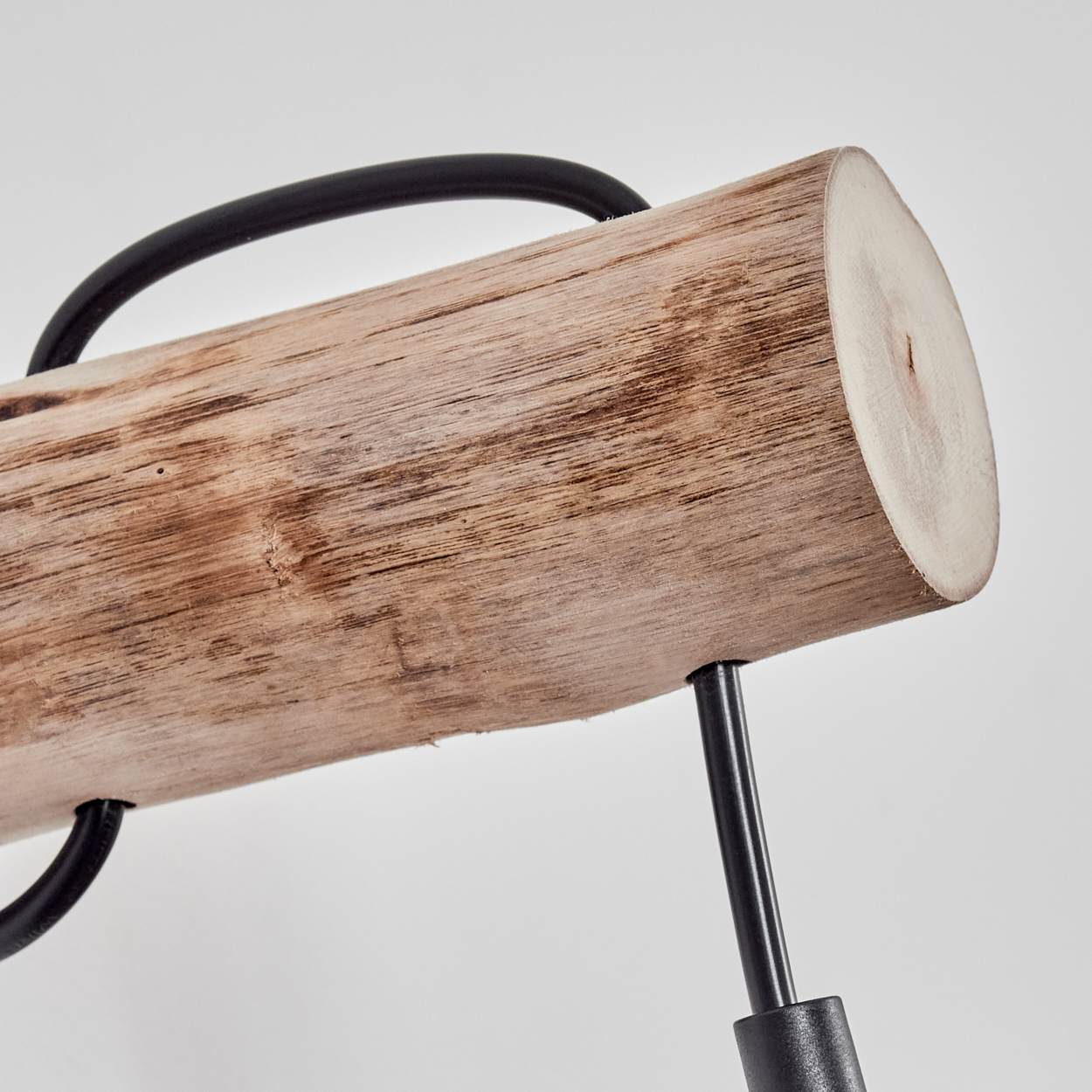 Ein Holzstamm mit schwarzen Metallstützen. Oben befindet sich ein schwarzes, gebogenes Rohr. Der Hintergrund ist einfarbig weiß.