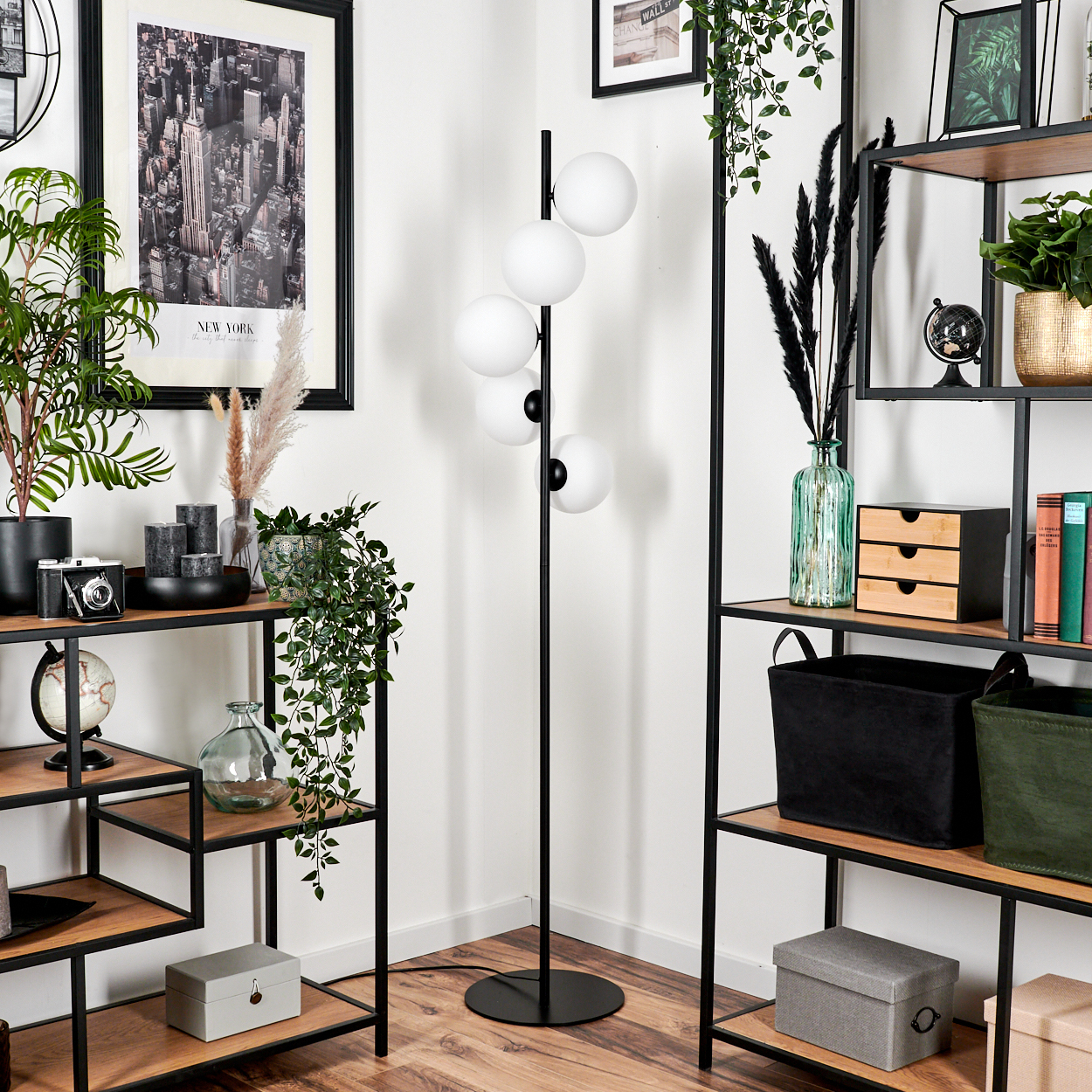 Zimmerecke mit Regalen, schwarze Lampe mit weißen Kugeln, verschiedene Dekorationen wie Pflanzen und ein New York-Bild.