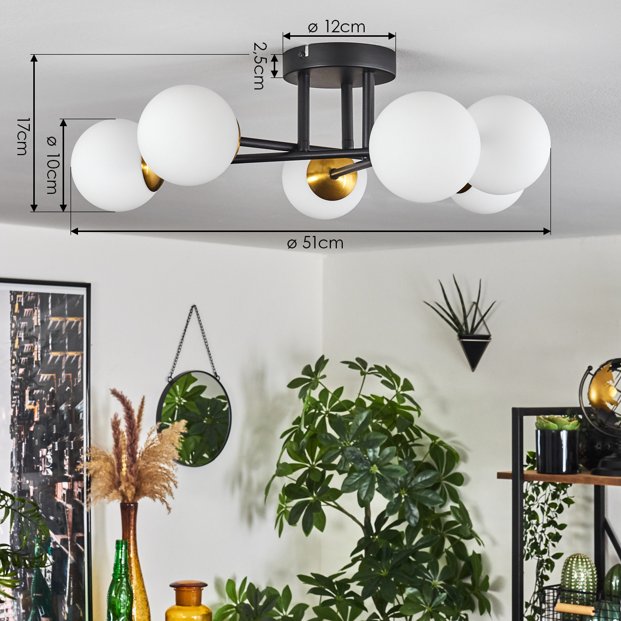 Eine schwarze Deckenlampe mit weißen Kugeln, goldenen Akzenten und beschrifteten Abmessungen. Pflanzen, ein Spiegel und Dekorationen darunter.