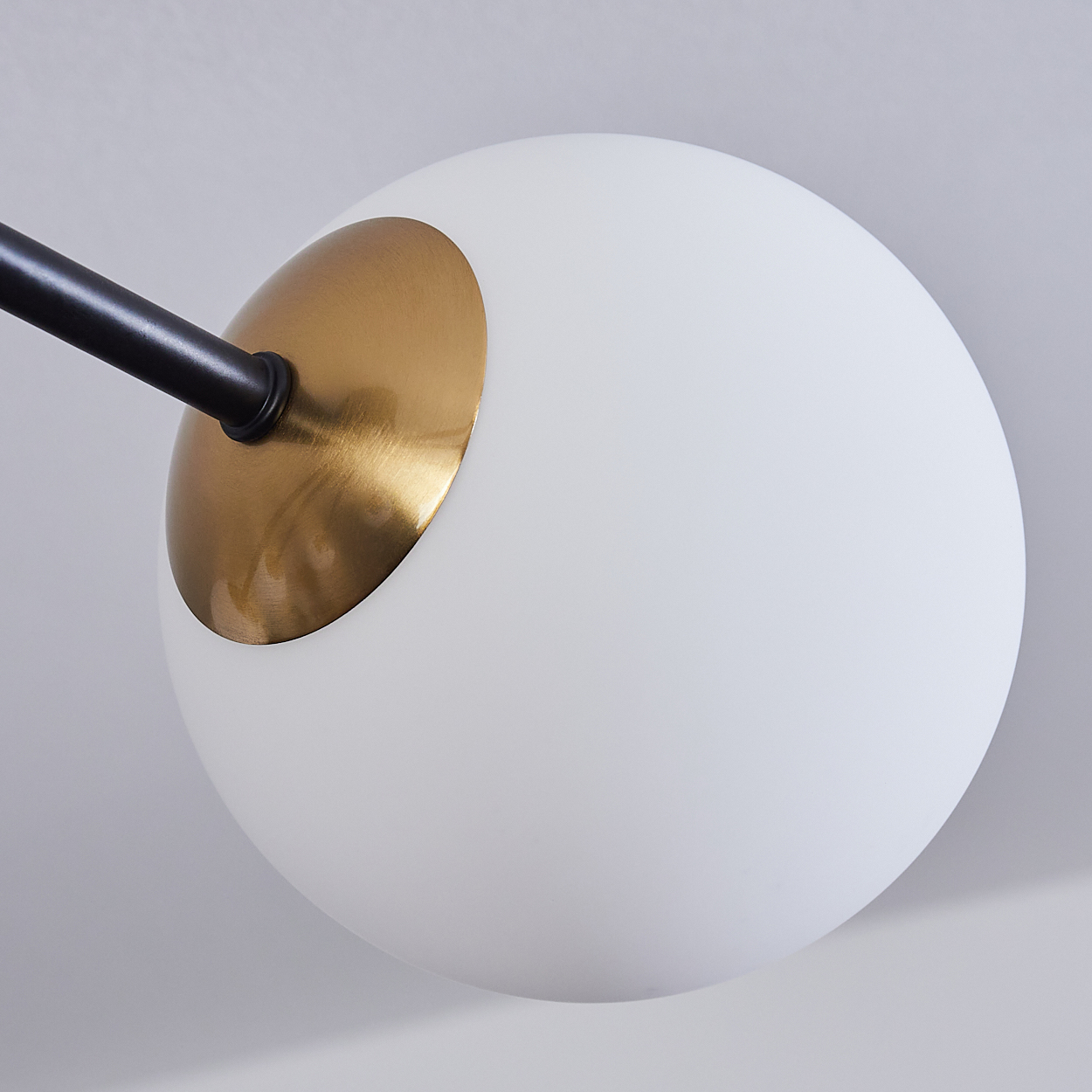 Nahaufnahme einer modernen Lampe. Sie hat eine weiße Kugel mit goldenem Akzent und einen schwarzen Arm, der sich davon erstreckt.