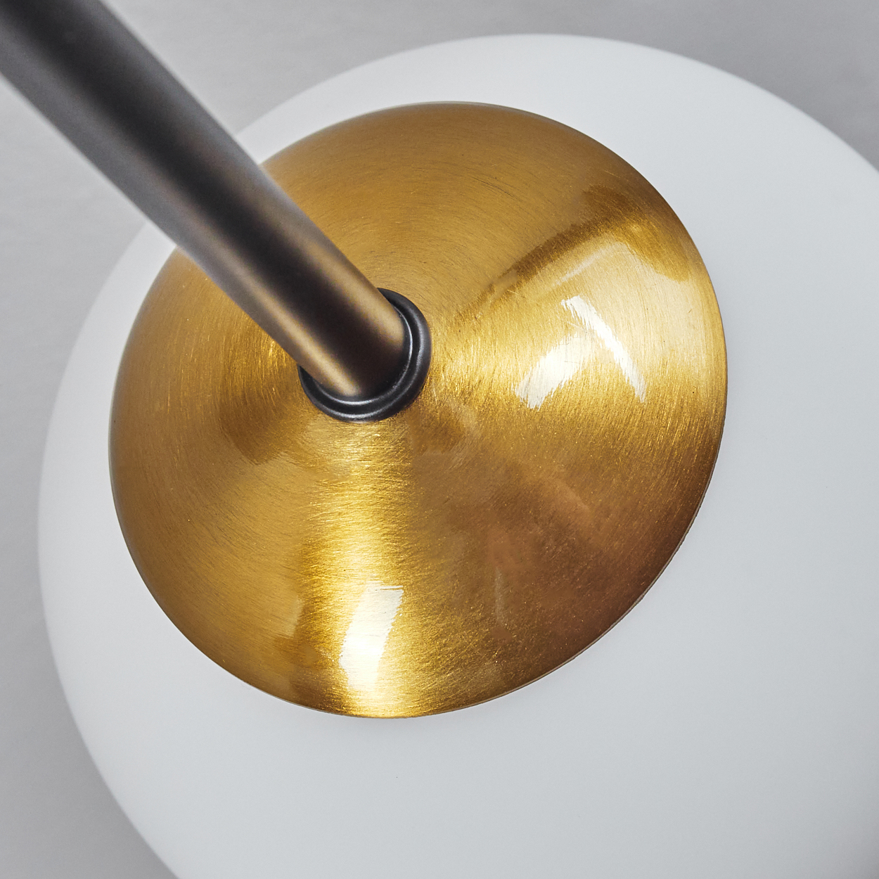 Nahaufnahme einer Lampe. Merkmale: goldfarbener, kreisförmiger Schirm mit dunklem Stiel. Der Hintergrund ist weiß und unscharf.