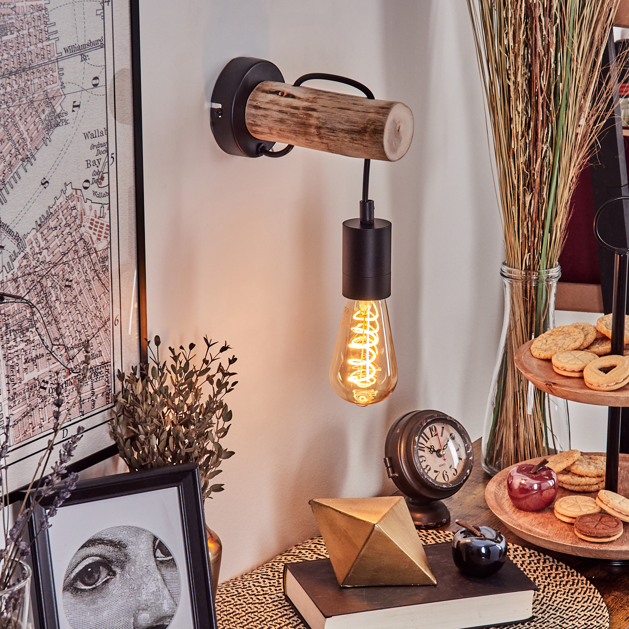 Eine Wandlampe mit Holzbalken und dekorativer Glühbirne, neben einer Karte, Keksen, einer Uhr und anderen Dekorationen.