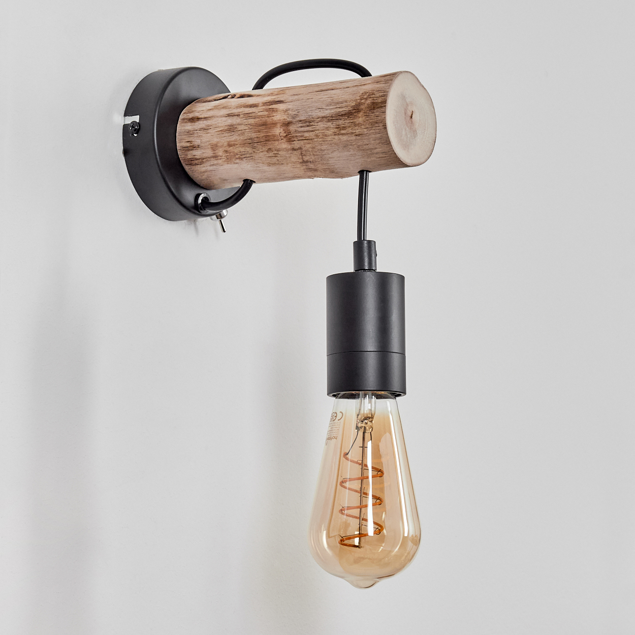 Eine Wandlampe mit Holzstamm, schwarzen Metallteilen und einer Glühbirne im Vintage-Stil vor weißer Wand.