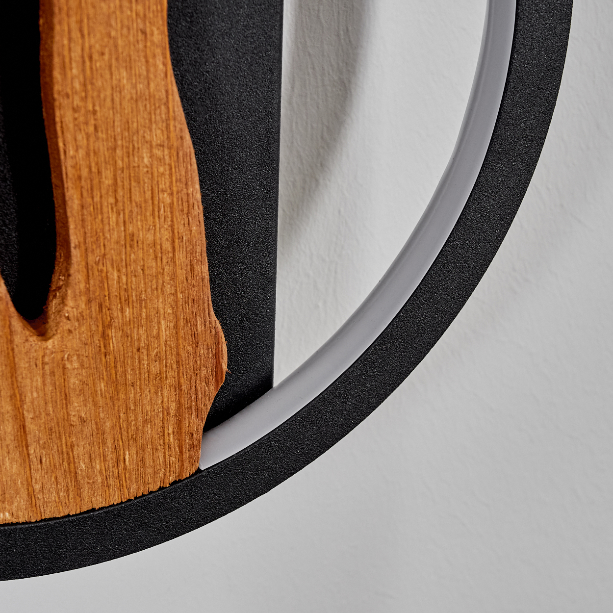 Nahaufnahme einer Wandkunst aus Holz und Metall. Eine braune Holzform ist an einem schwarzen Metallrahmen befestigt, mit einem grauen Ring.