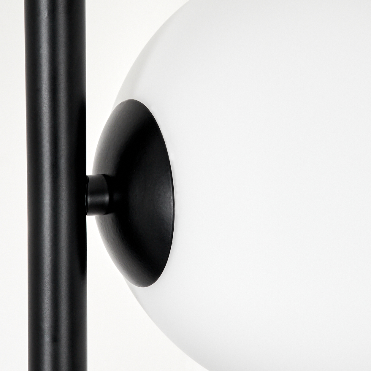 Eine moderne Lampe mit einem schwarzen Metallpfosten und einer großen weißen Kugel. Die Kugel ist mit einer schwarzen Halterung an der Stange befestigt.