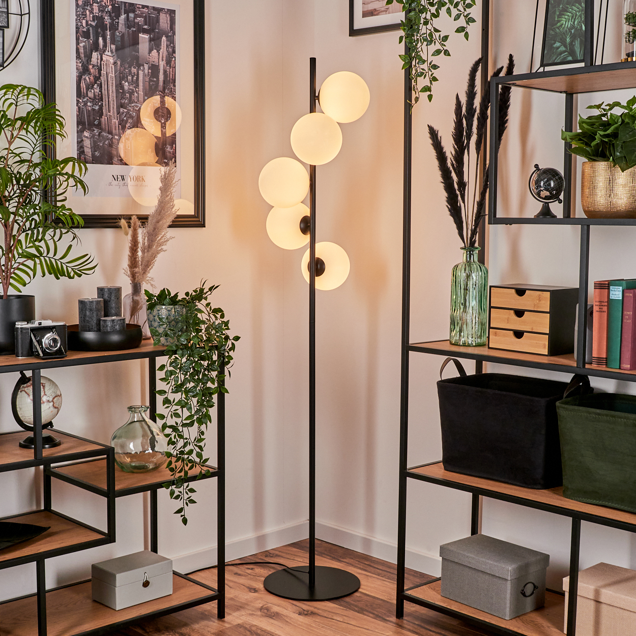 Modernes Wohnzimmer mit Stehlampe und Regalen. Regale sind mit Pflanzen, Büchern und Dekorationsartikeln gefüllt. Ein New-York-Poster hängt an der Wand.