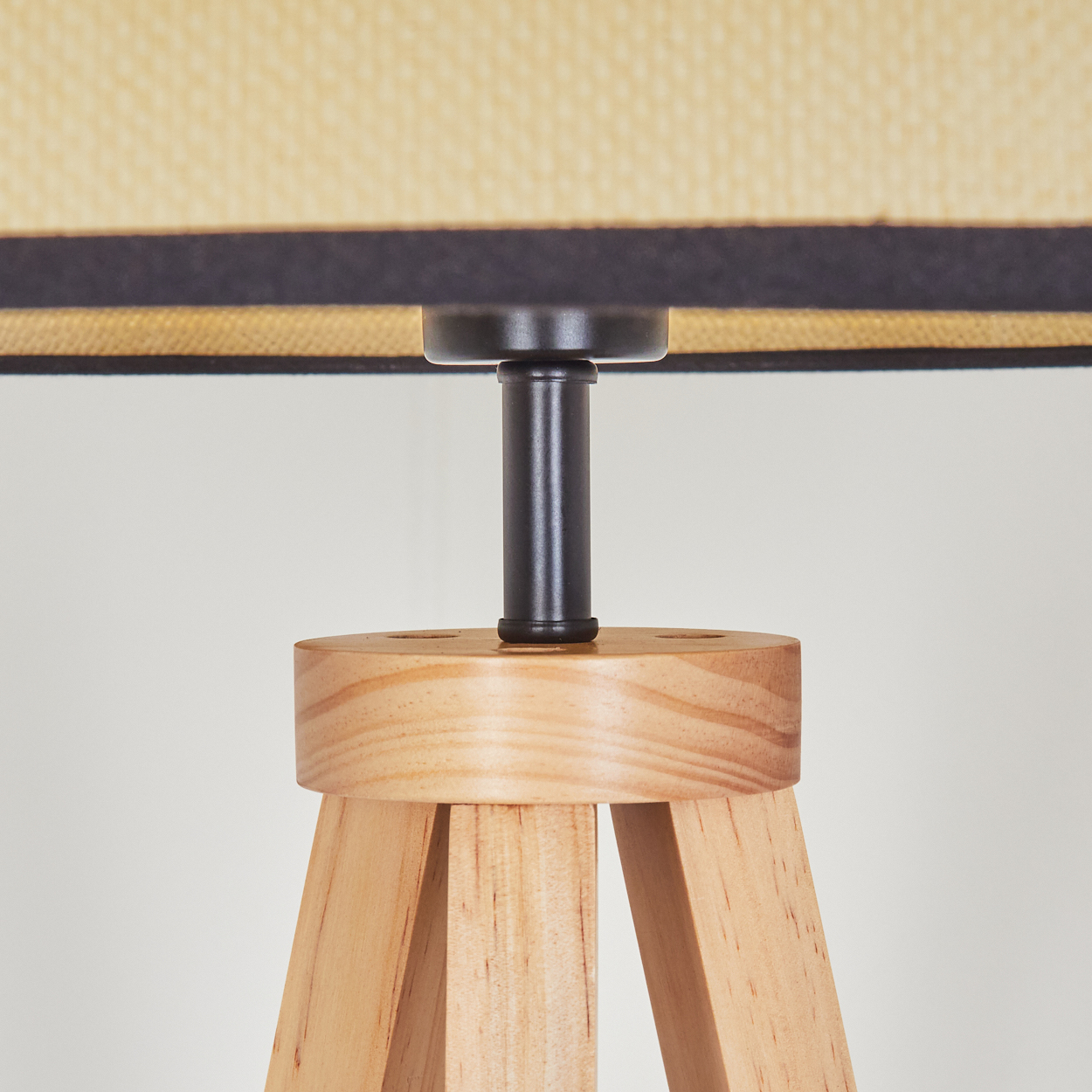 Nahaufnahme einer Lampe. Sie hat einen Holzfuß und eine schwarze Metallstange. Der Lampenschirm ist beige mit einem schwarzen Rand.