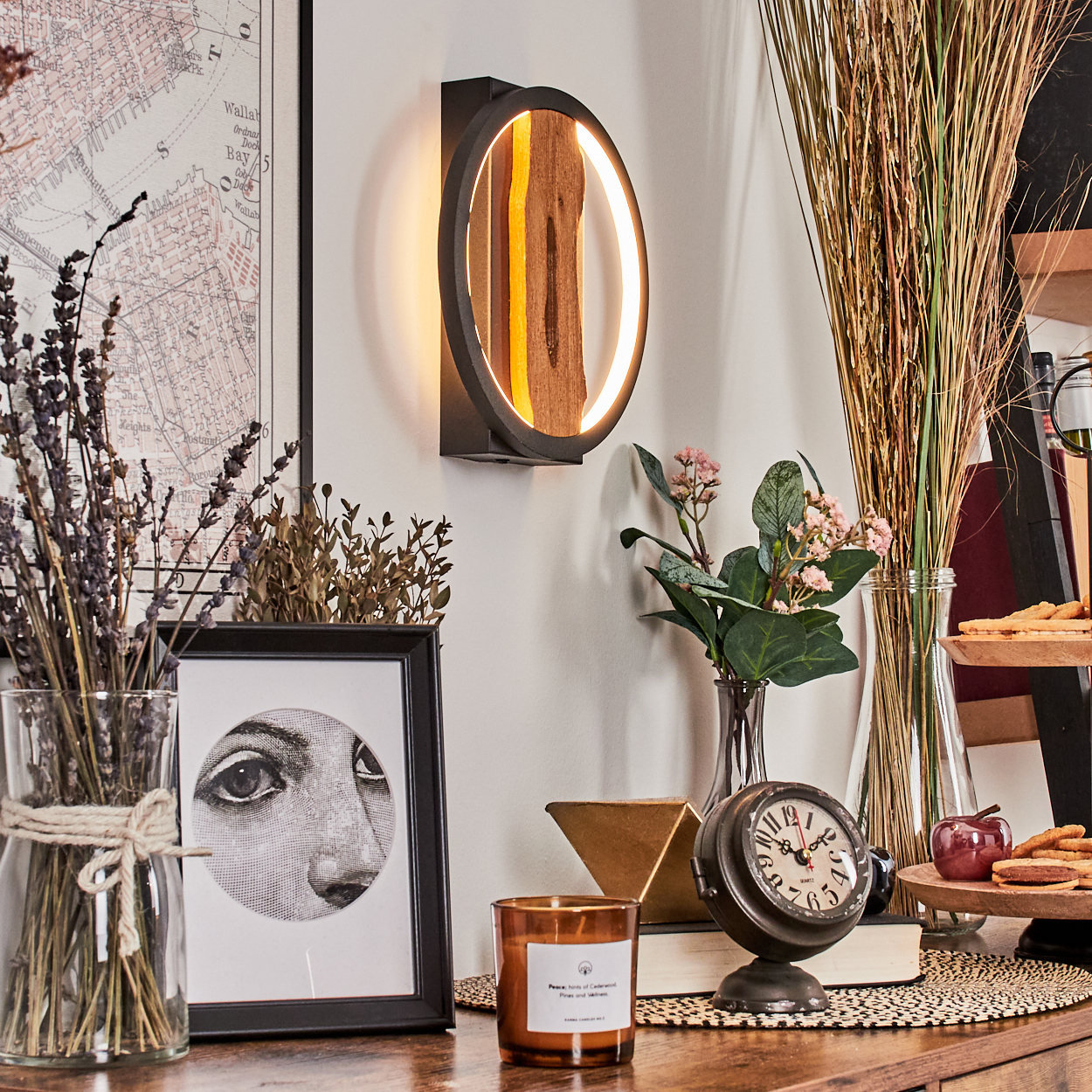 Eine stilvolle Innenszene mit Wandlampe, Uhr, Bild, Blumen und Dekorationsartikeln auf einer Holzoberfläche.