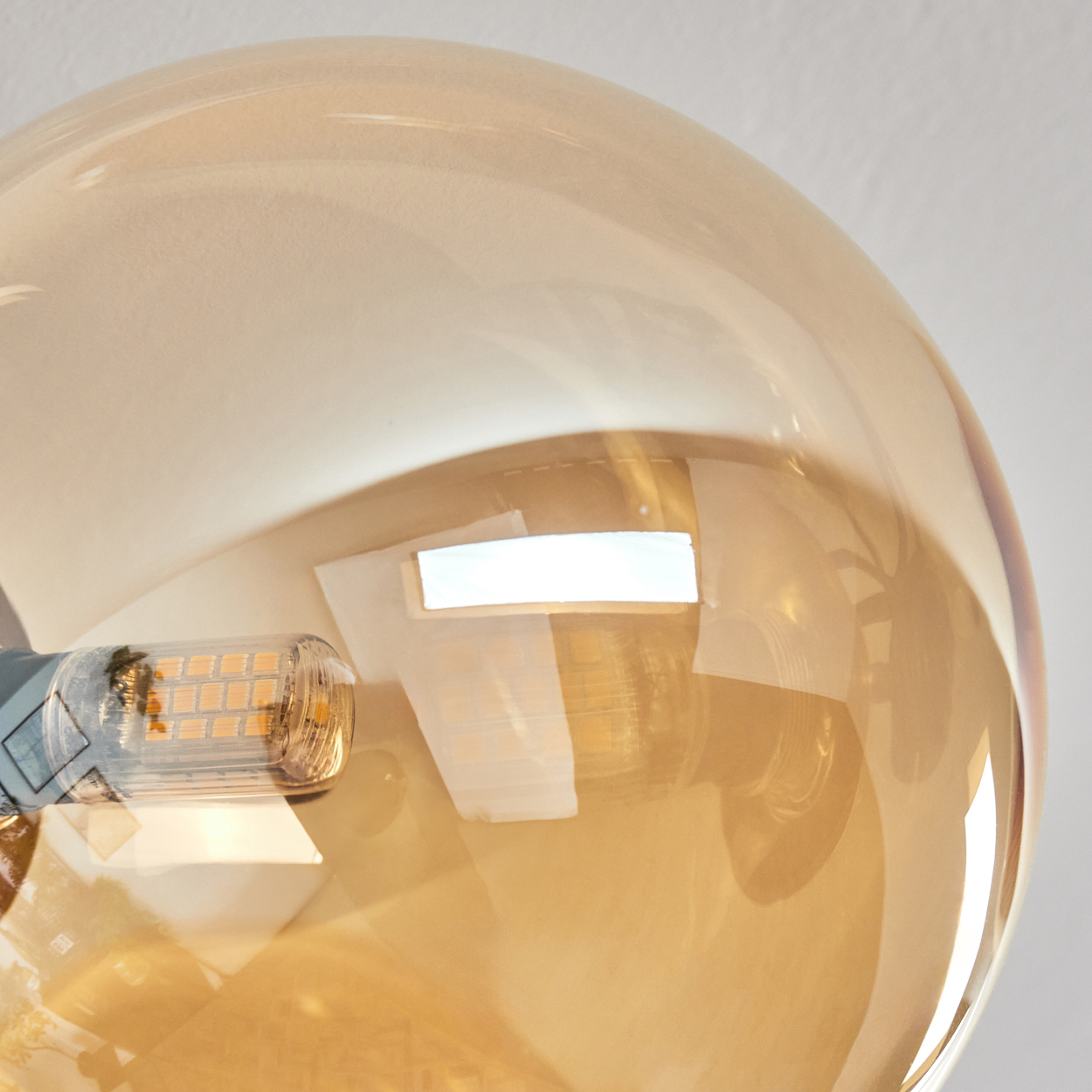 Nahaufnahme einer Glühbirne. Die Glühbirne ist aus bernsteinfarbenem Glas, das Licht reflektiert. Die Fassung ist silberfarben, mit hellem Licht.