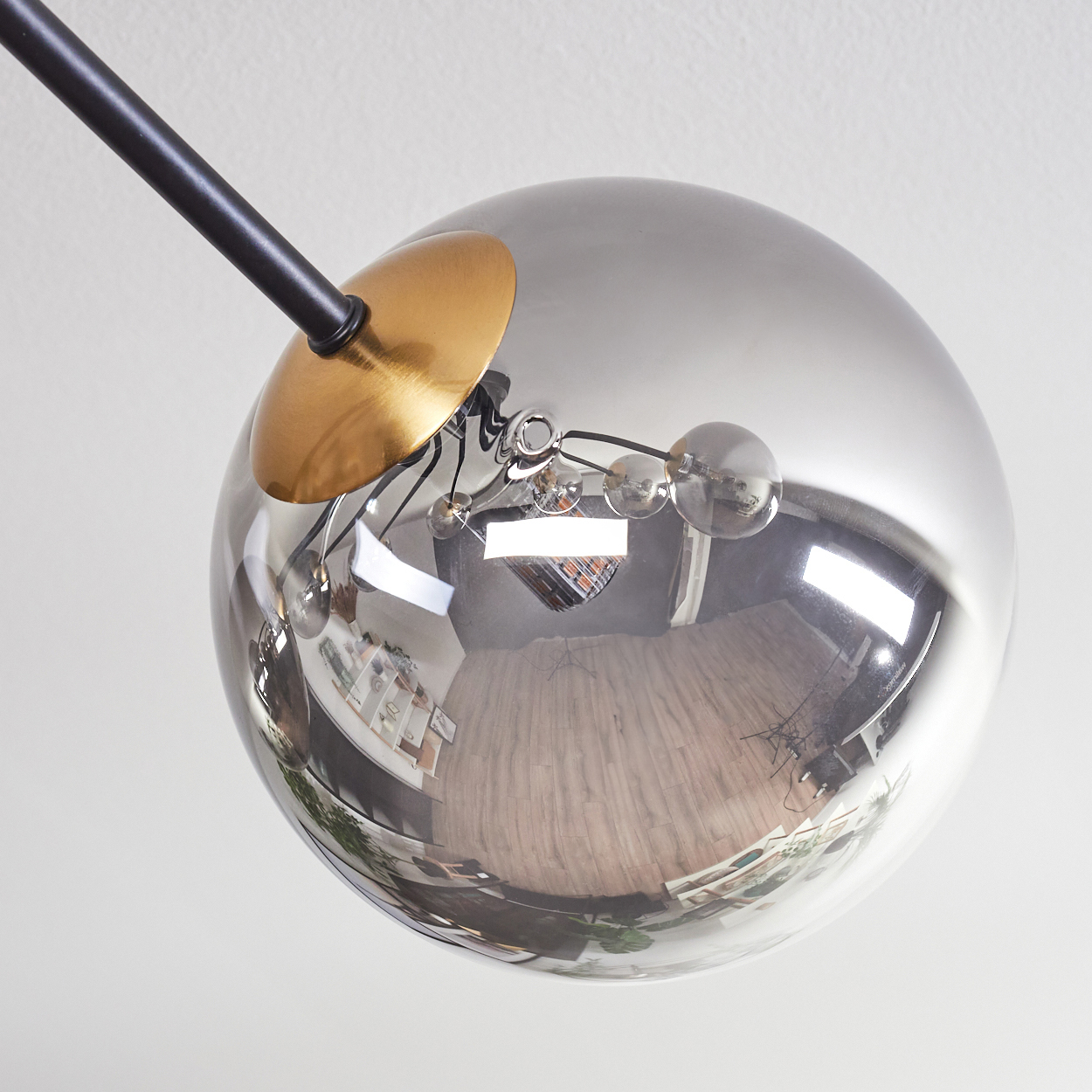 Eine moderne Leuchte mit einer großen, reflektierenden, silbernen Kugel und einem schwarzen Arm. Die Kugel reflektiert einen Raum.