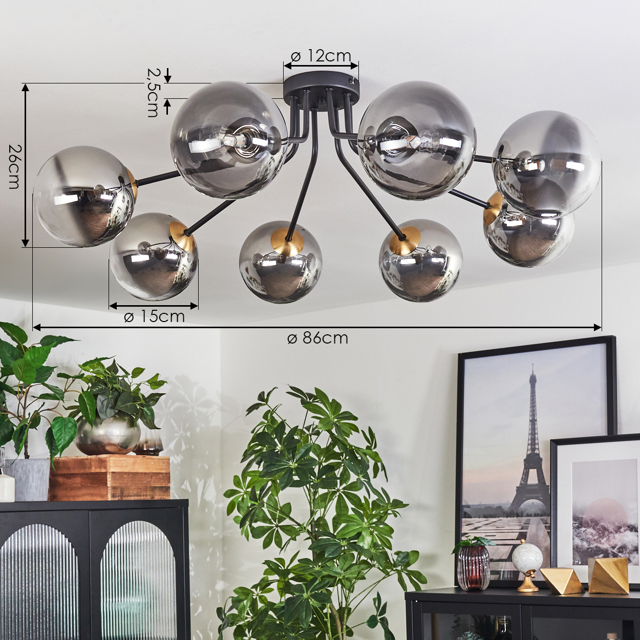 Moderne Deckenlampe mit acht kugelförmigen Glasschirmen. Der Raum hat Pflanzen, schwarze Möbel und gerahmte Bilder.