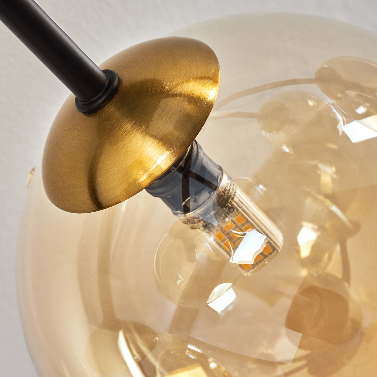 Nahaufnahme einer modernen Leuchte mit goldfarbenem Schirm, klarer Glaskugel und einer sichtbaren Glühbirne.