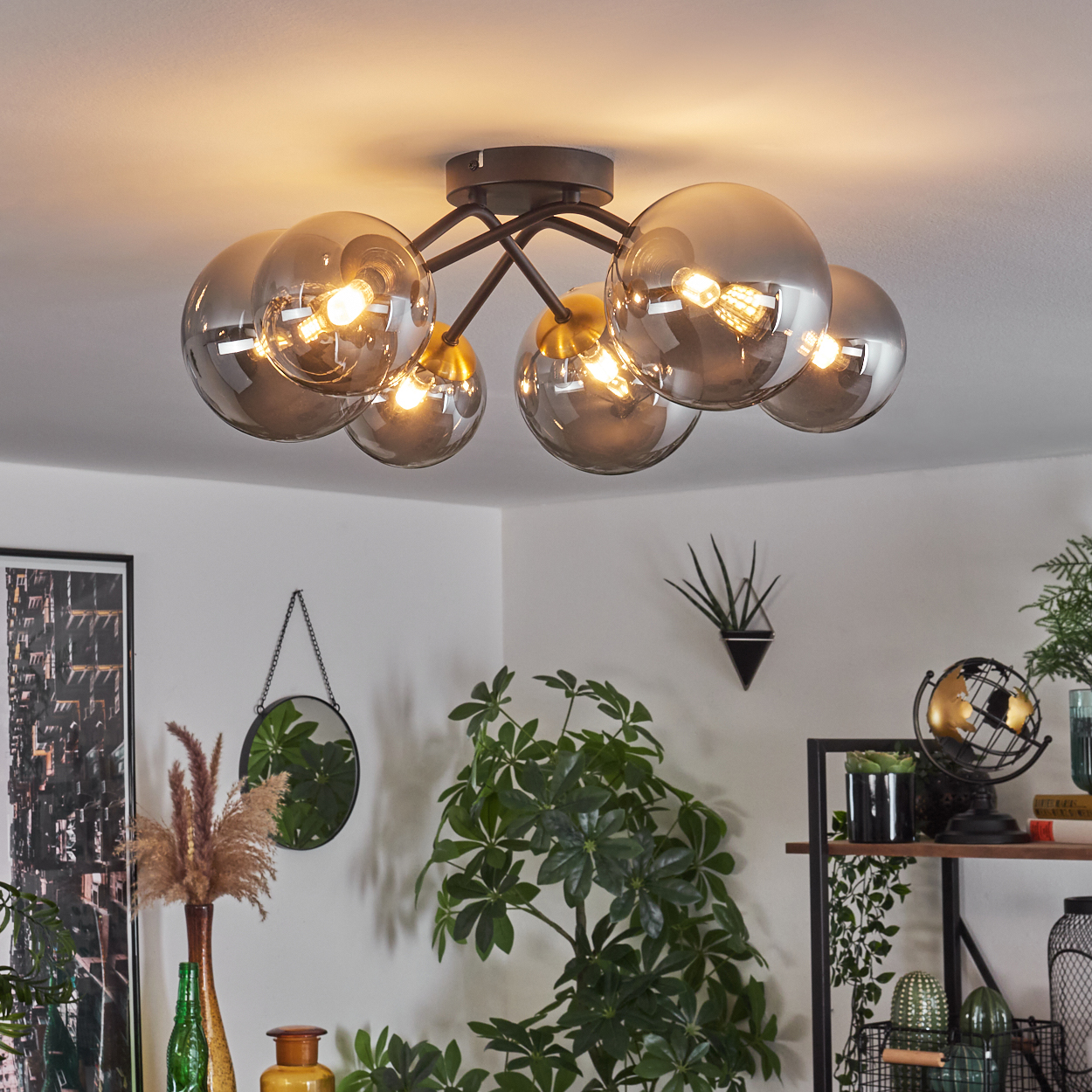 Eine moderne Deckenleuchte mit sechs Glaskugeln, die einen Raum mit Pflanzen, einem Spiegel und Dekoration beleuchtet. Warme Beleuchtung schafft eine gemütliche Atmosphäre.