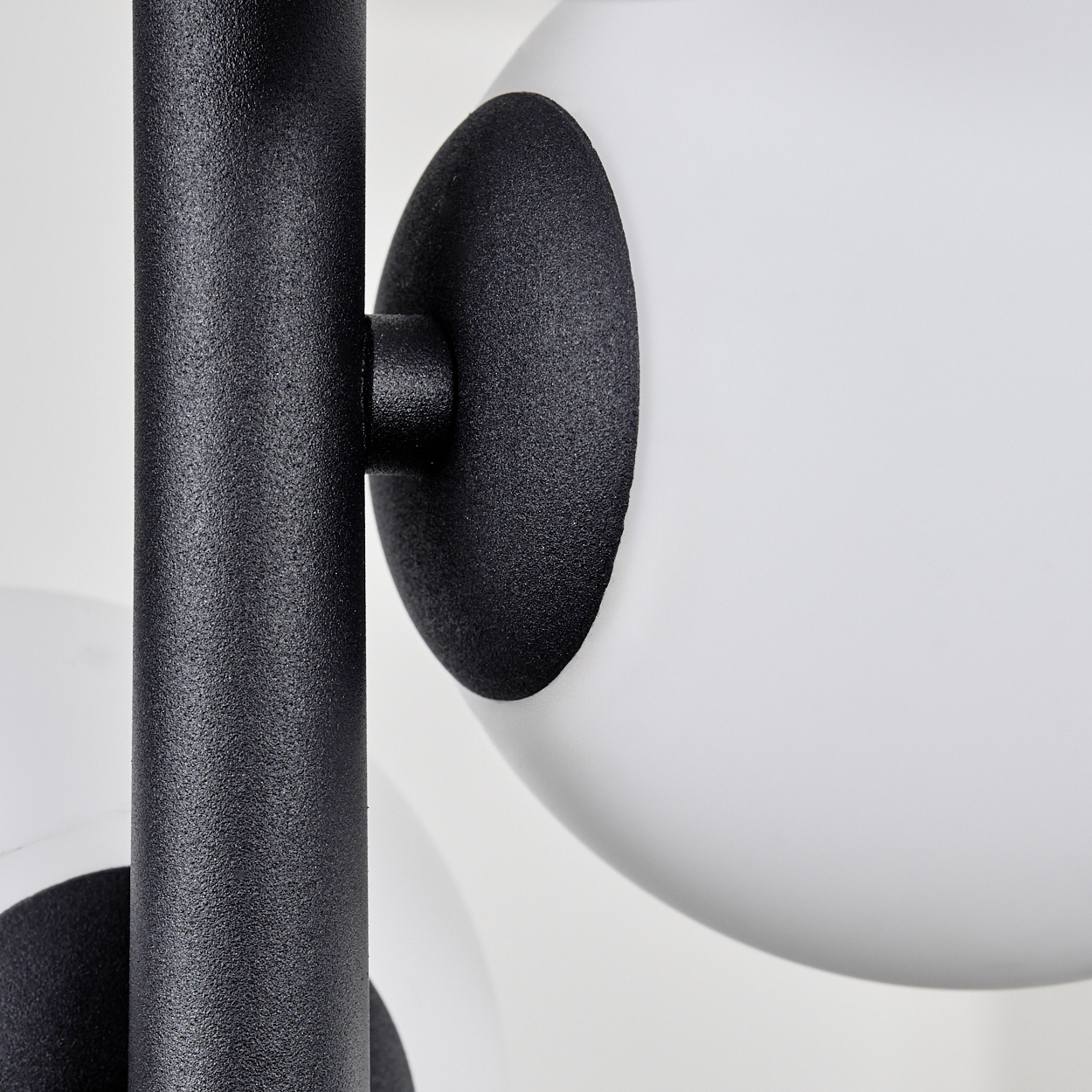 Nahaufnahme einer Lampe mit schwarzem Metallrahmen und weißen, kugelförmigen Lampenschirmen. Der Hintergrund ist weiß.