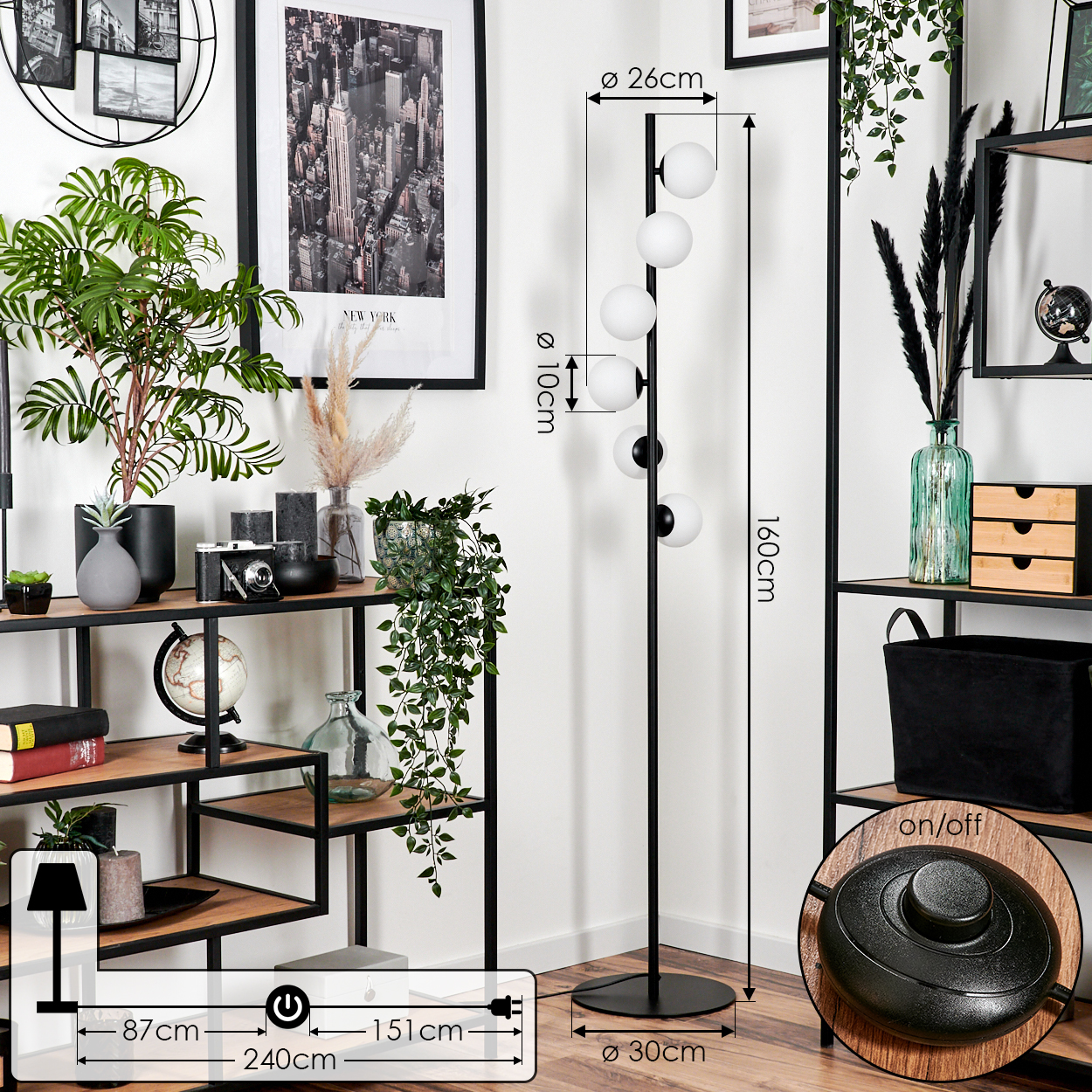 Ein Raum mit Regalen, Pflanzen und einer Stehlampe. Die Lampe hat weiße Kugellampen. Ein New York City-Druck hängt an der Wand.