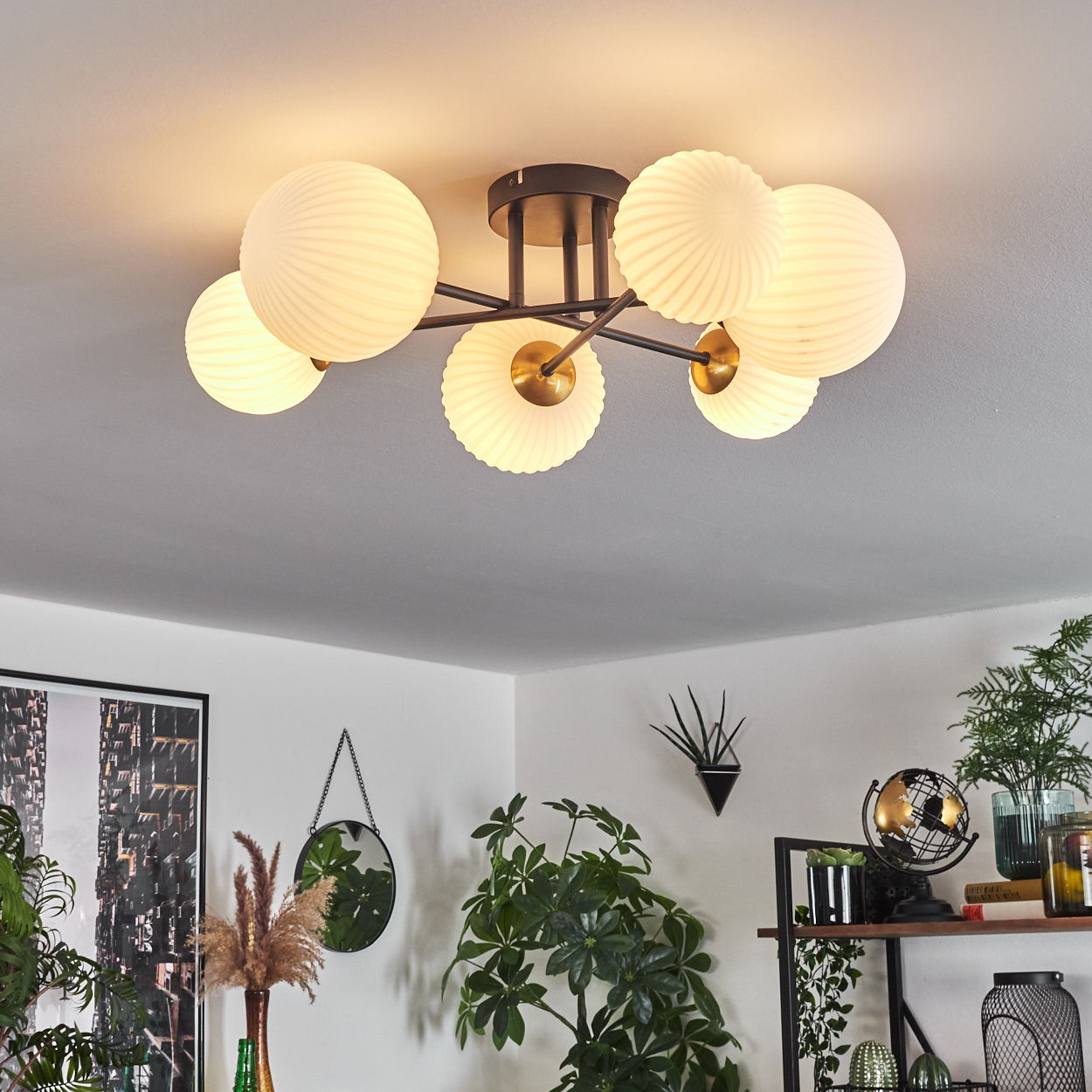 Eine moderne Deckenleuchte mit kugelförmigen Schirmen, umgeben von Pflanzen und Dekoration. Der Raum hat eine weiße Decke und Wände.