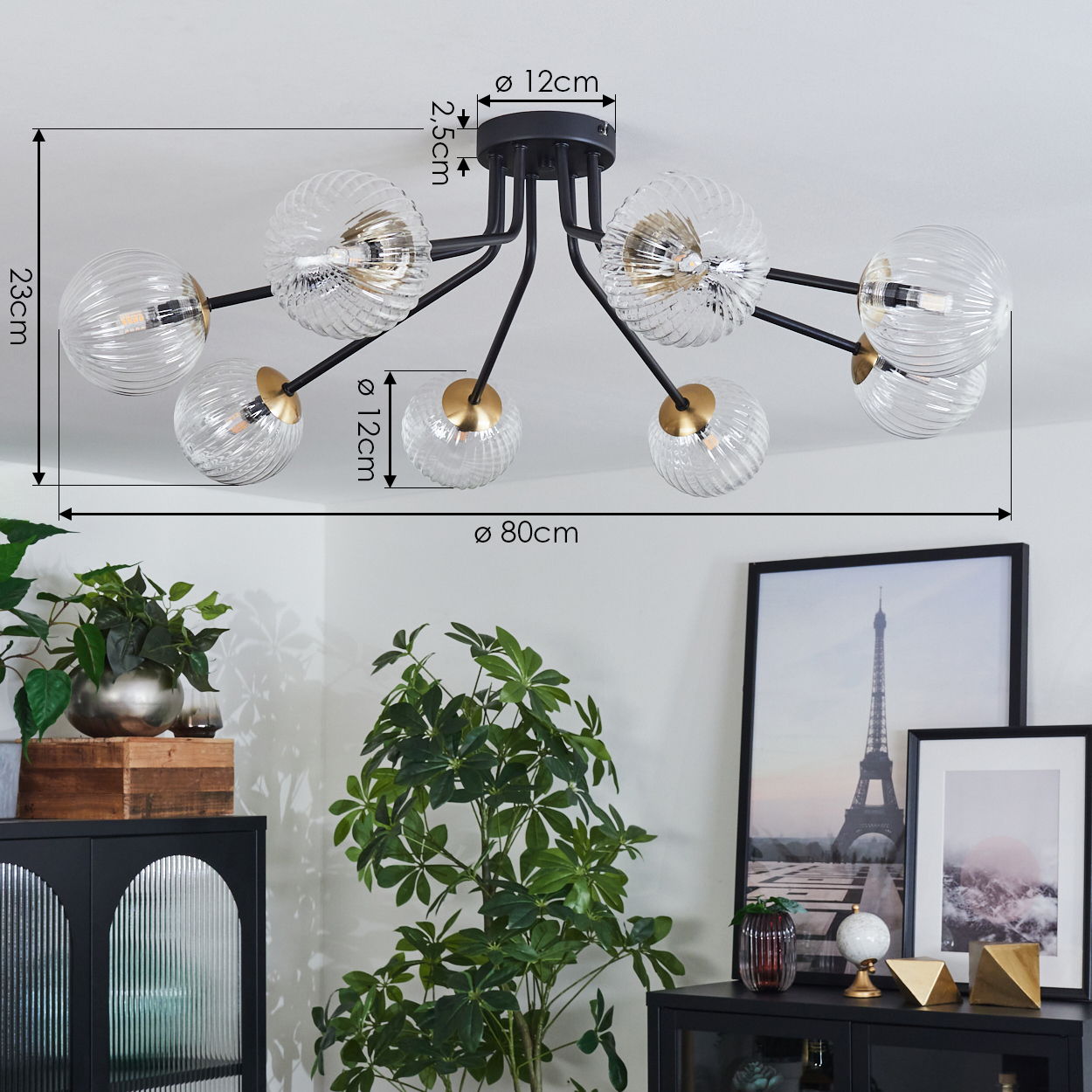 Eine Deckenlampe mit Glaskugeln. Maße sind angegeben. Die Szene umfasst Pflanzen, einen schwarzen Schrank und gerahmte Bilder des Eiffelturms.