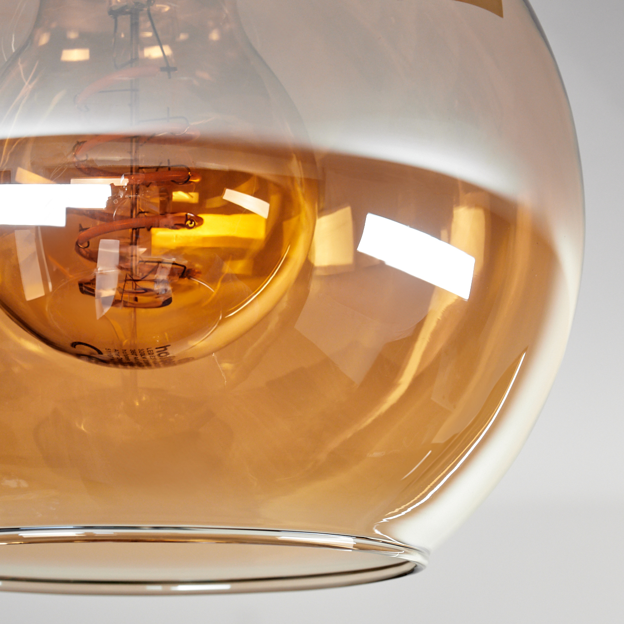 Nahaufnahme einer Glühbirne in einem Glasschirm. Die Glühbirne hat einen warmen, orangen Farbton, und der Glühfaden ist sichtbar.