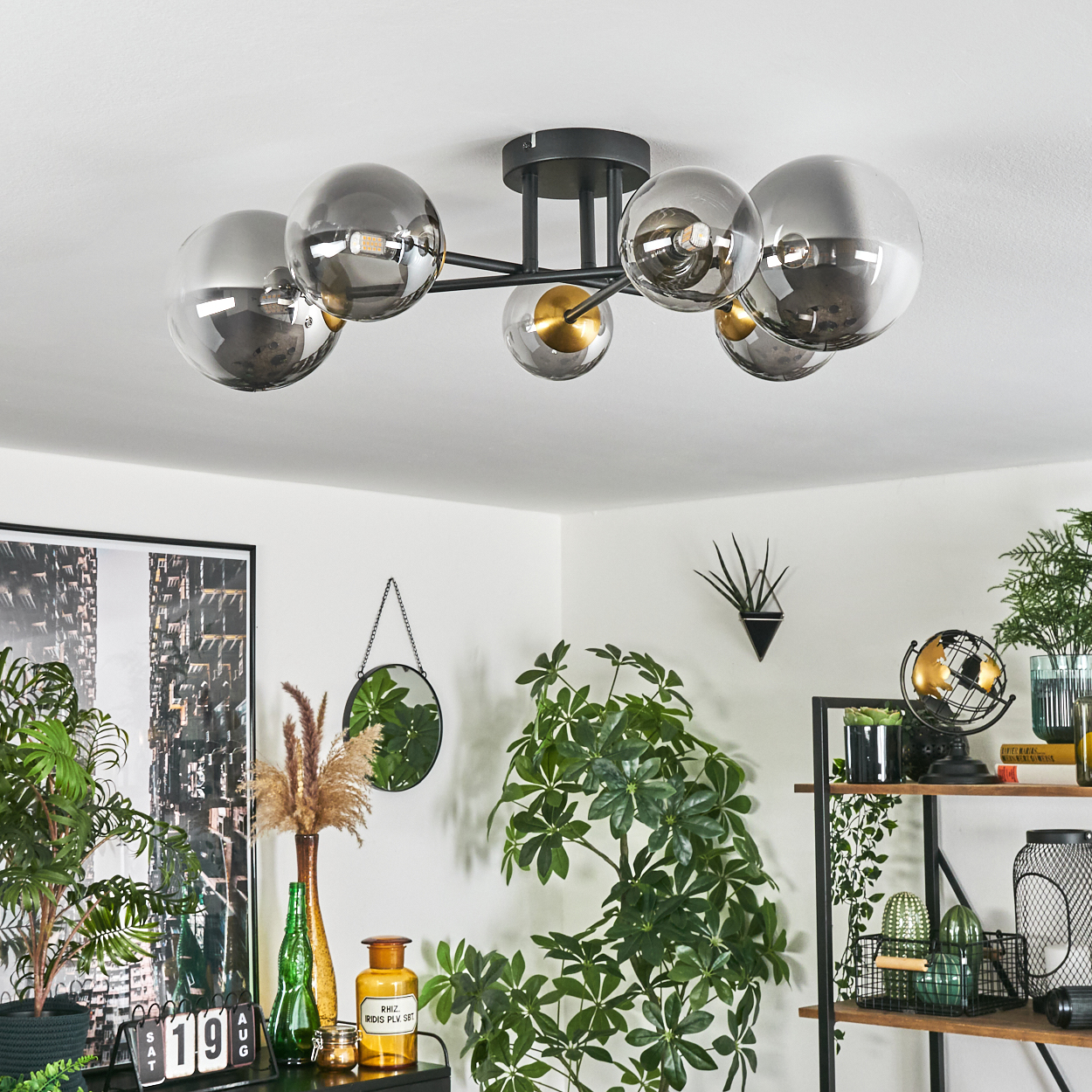 Eine Deckenlampe mit Glaskugeln, Pflanzen und Regalen mit Dekoration, darunter ein Globus, Pflanzen und ein Spiegel.